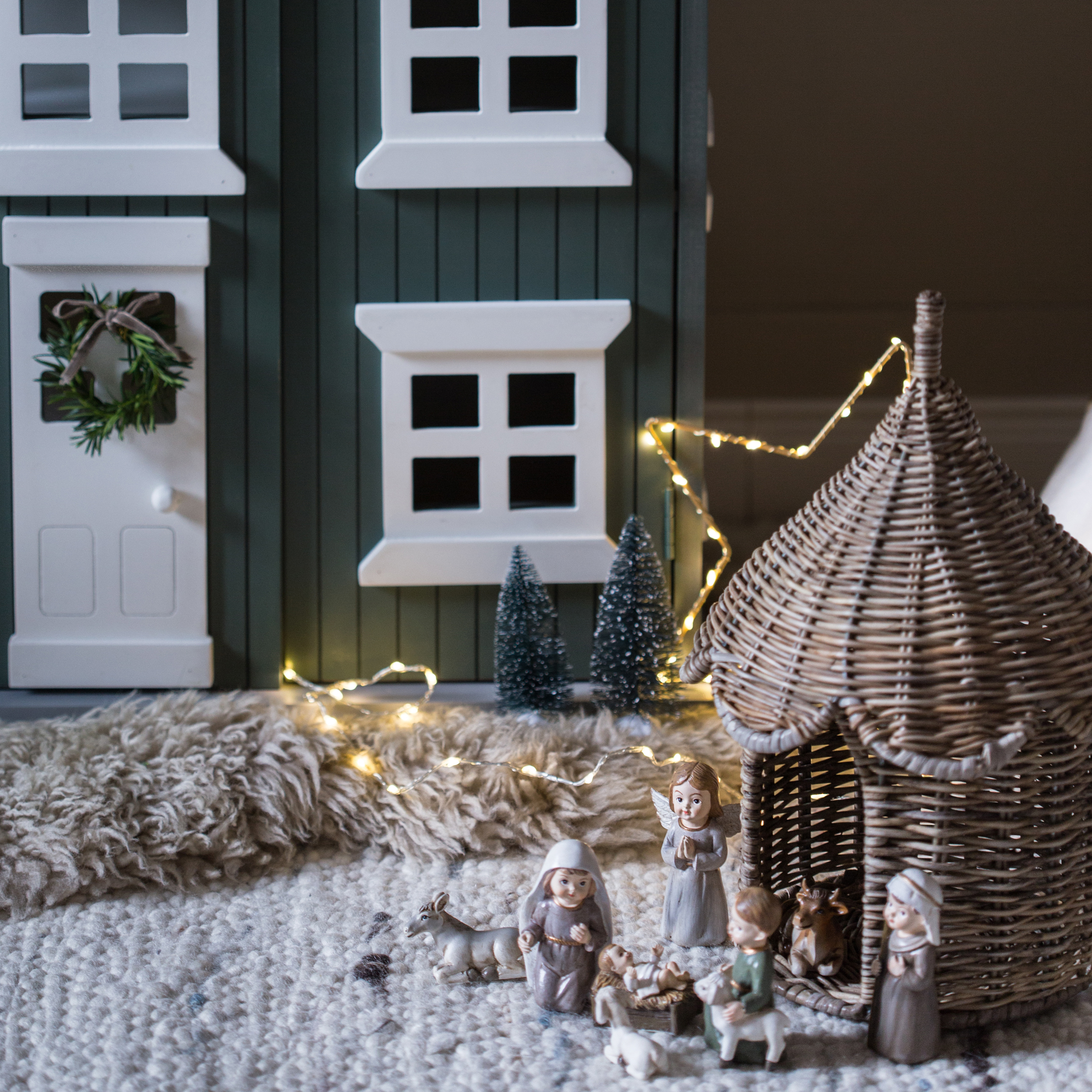 Weihnachtsdekoration mit Krippenfiguren und Korbkrippe auf Teppich mit LED-Lichterkette