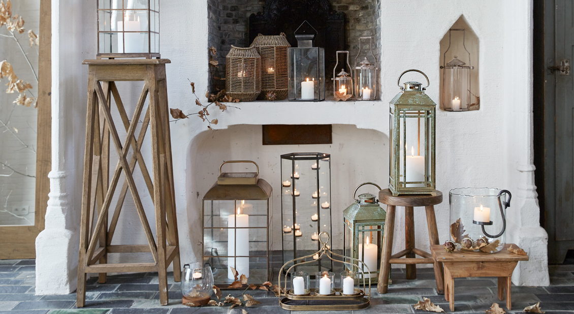Set aus Holz- und Metalllaternen mit weißen Kerzen vor weißem Kamin und Steinboden