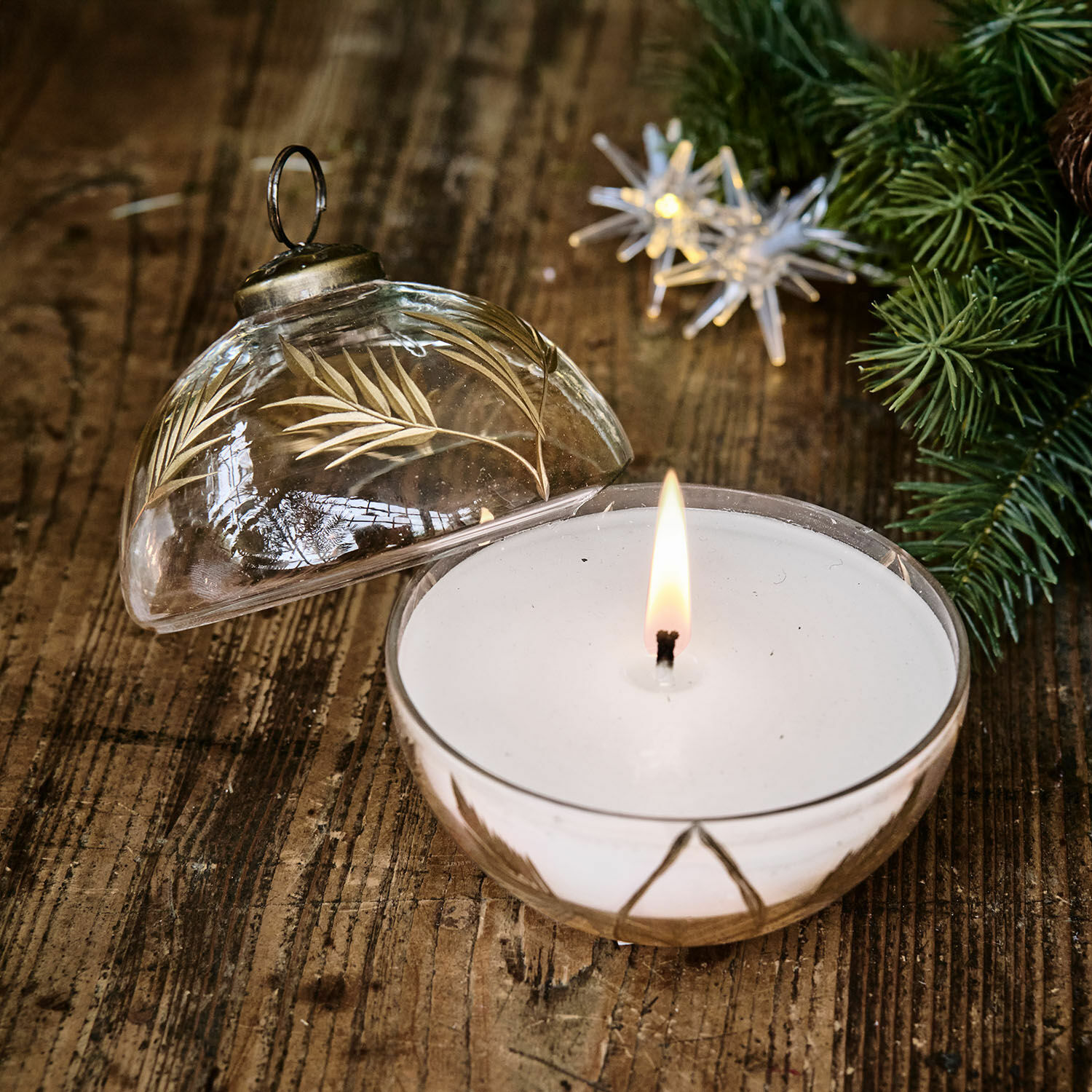 Duftkerze in klarem Glas mit goldenem Blattmuster auf rustikalem Holztisch dekorativ platziert