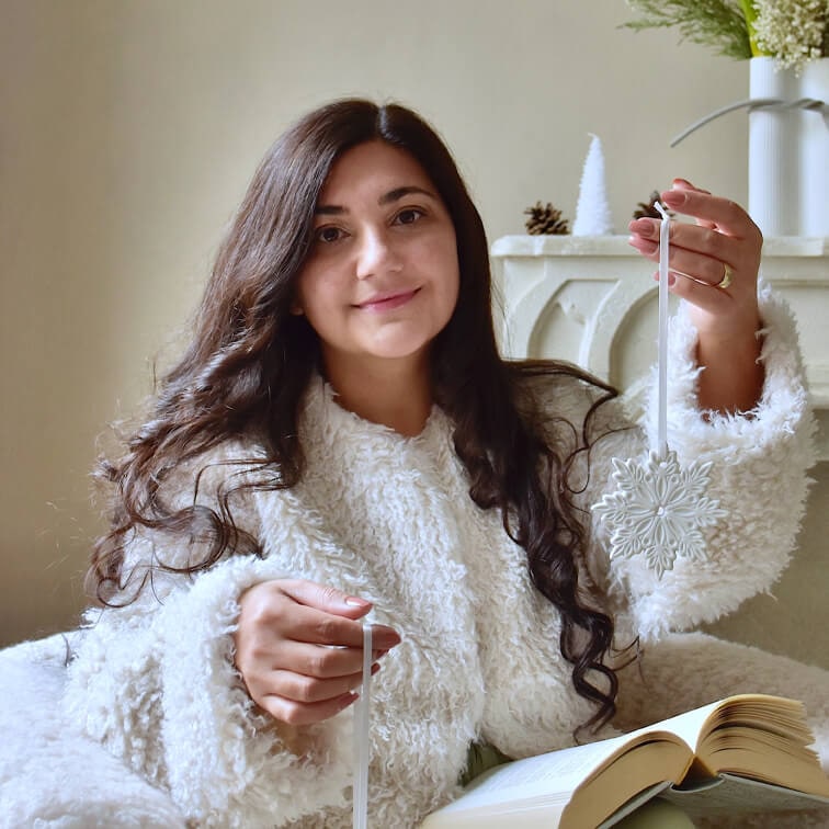 Frau in weißem flauschigem Pullover hält weißen Schneeflocken-Weihnachtsschmuck mit offenem Buch auf dem Schoß