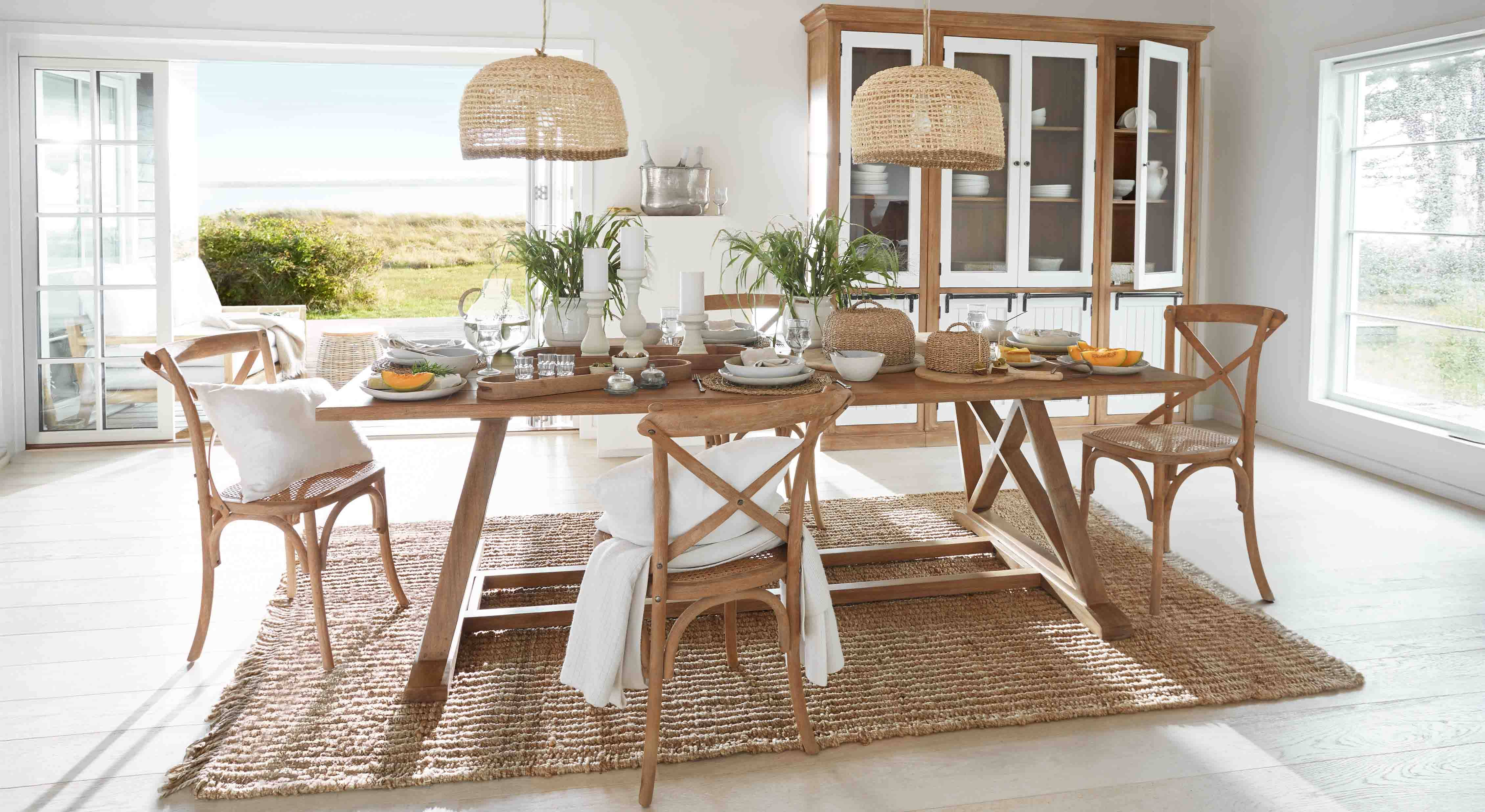 Esszimmer mit Holztisch und Rattanstühlen auf Naturteppich, Pflanzen und Korbhängelampen