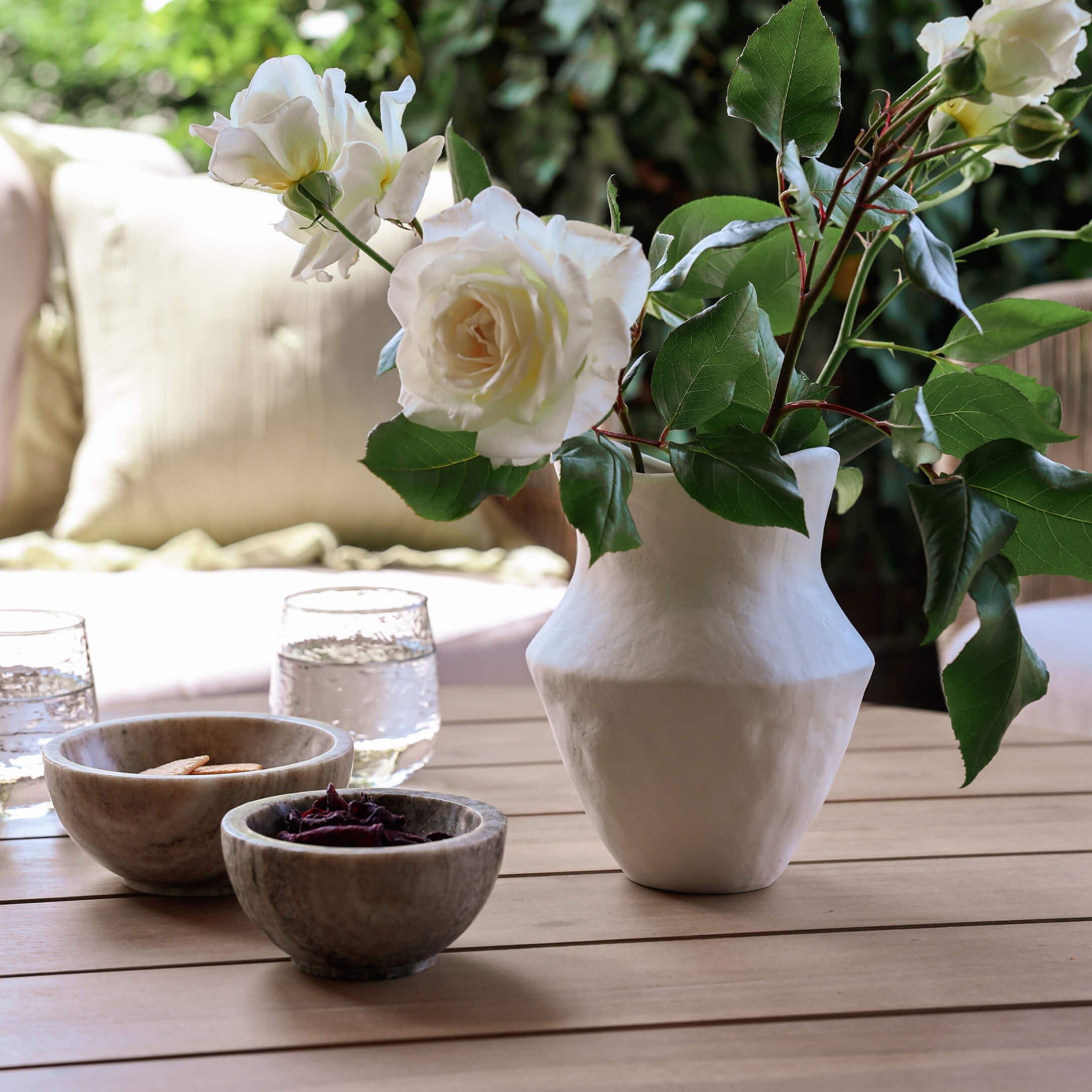 Weiße Keramikvase mit weißen Rosen auf Holztisch mit Schalen und Wassergläsern