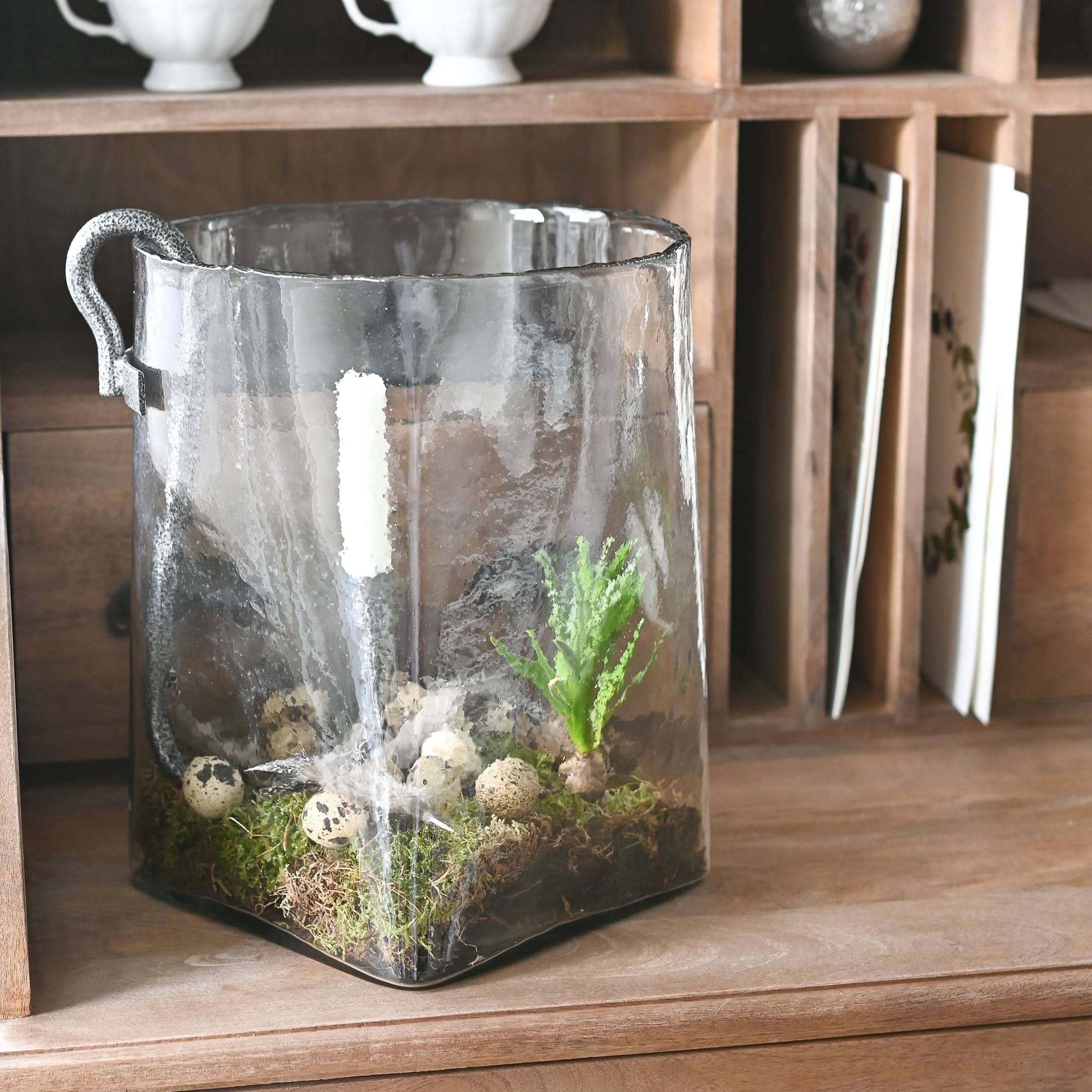 Transparenter Glasbehälter mit Griff, dekoriert mit Moos und Wachteleiern auf einem Holztisch