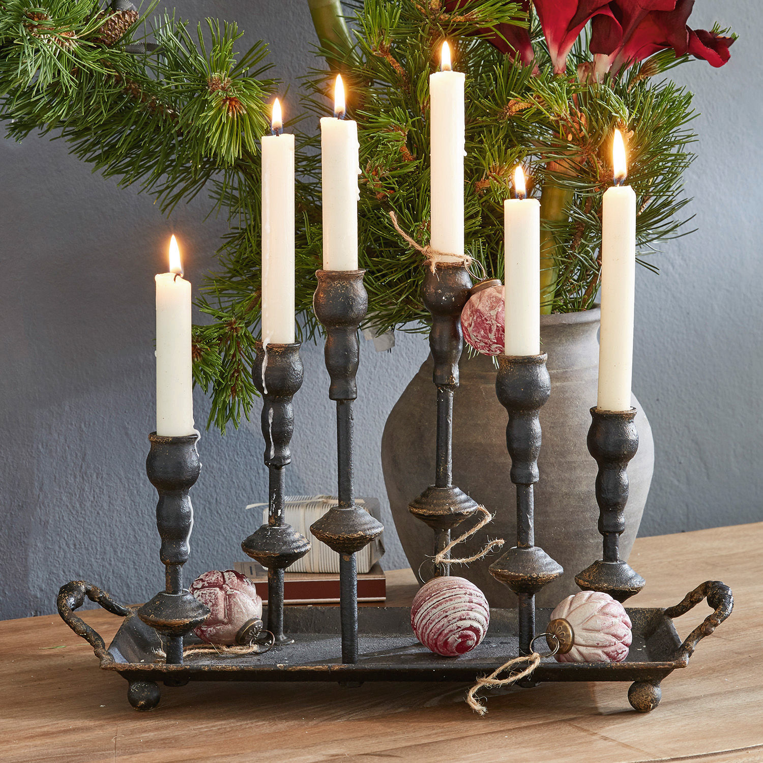 Schwarzer Metall-Kerzenhalter mit sechs weißen Kerzen und Weihnachtskugeln auf Holztisch