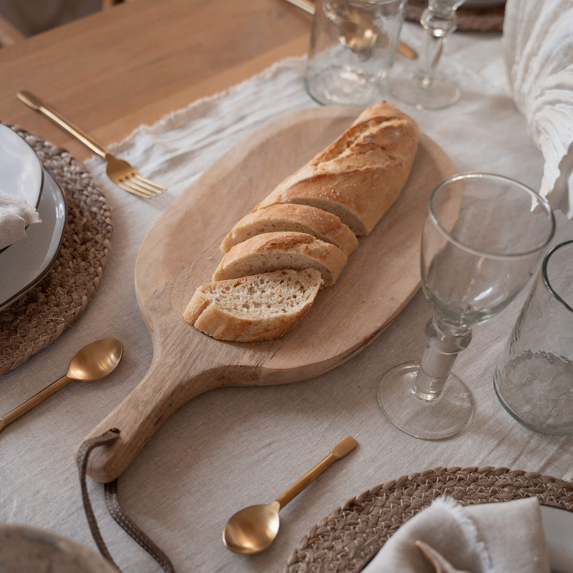 Holzschneidebrett mit geschnittener Baguette auf Tisch mit Geschirr und goldenen Bestecken