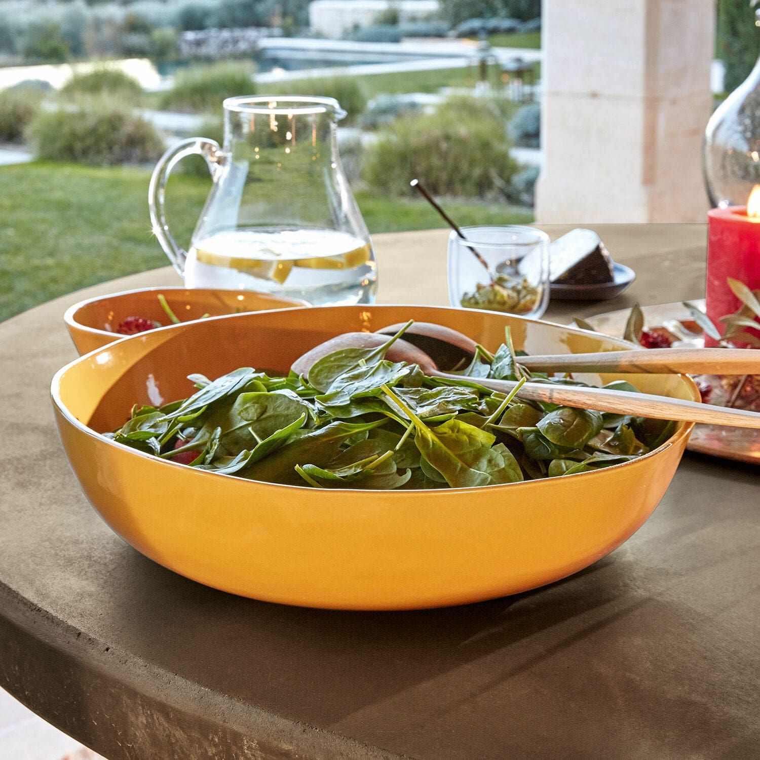 Gelbe Keramik-Salatschüssel mit Holzbesteck auf Gartentisch im Freien
