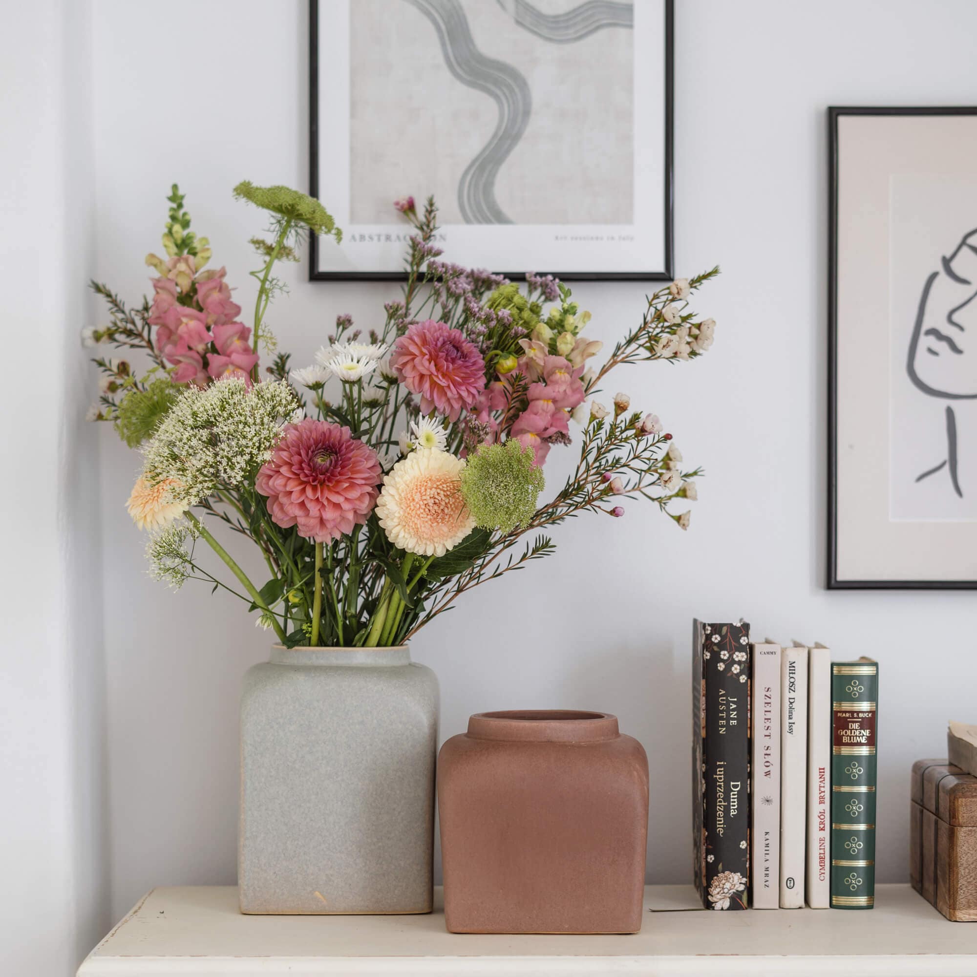 Zwei keramische Vasen in Grau und Braun auf weißem Tisch mit Blumenstrauß und Büchern