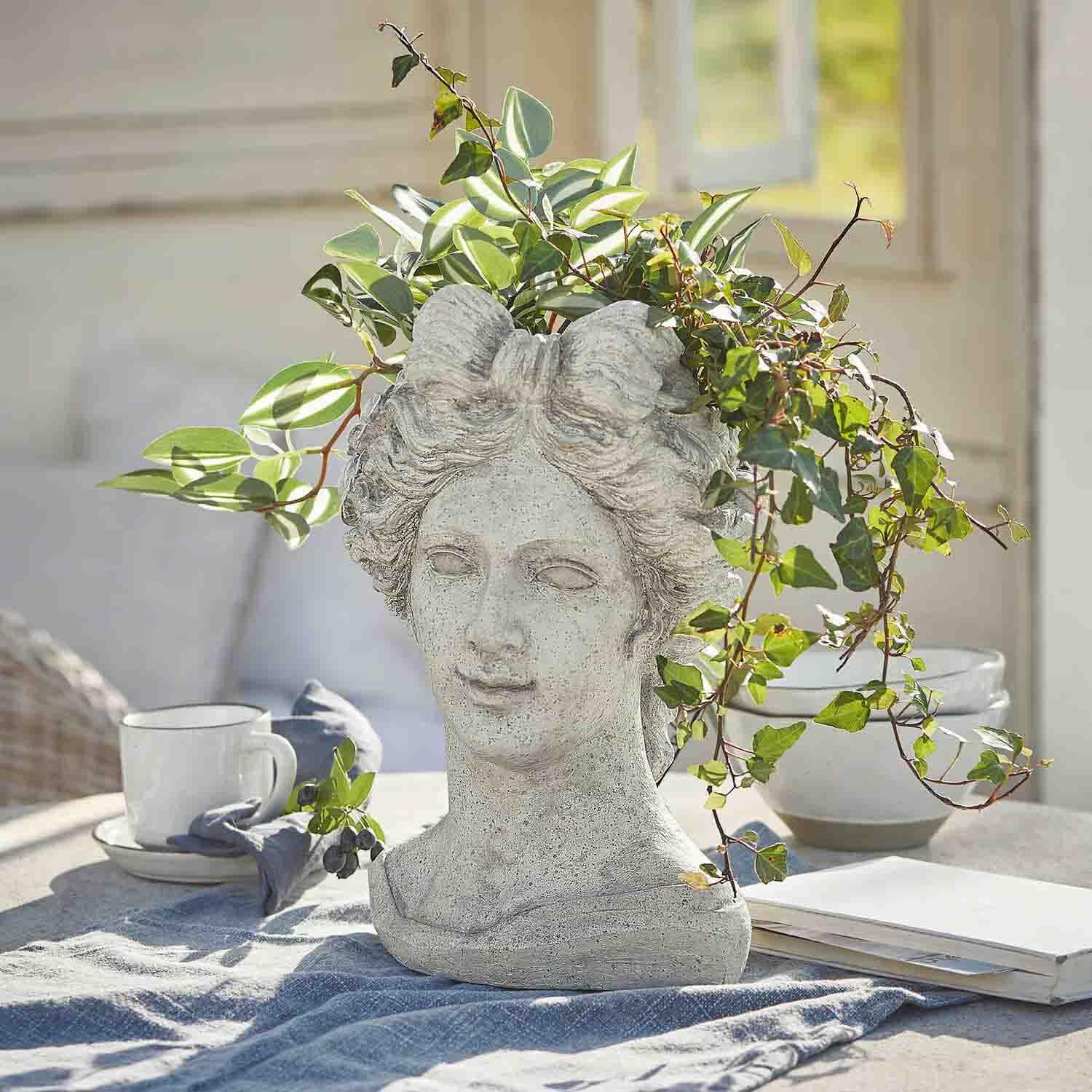 Blumentopf in Form eines Frauenkopfs aus grauem Stein mit grünen Pflanzen, Gartendekoration