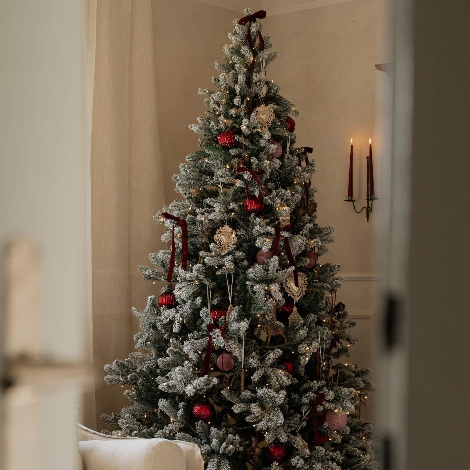 Künstlicher Weihnachtsbaum mit weißem Schneeeffekt und roten Kugeln, festliche Wohnraumdekoration