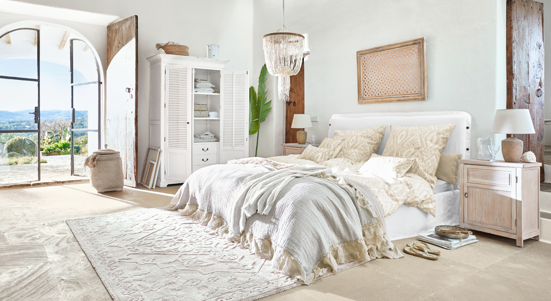 Helles Schlafzimmer mit weißem Bett, beiger Bettwäsche und rustikalen Holzmöbeln