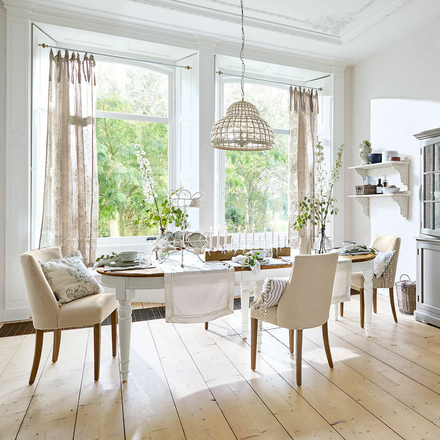 Esstisch Pinecrest Esszimmer mit weißem Holztisch und beigen Stühlen auf hellem Holzboden, Dekorationen und Korbhängeleuchte