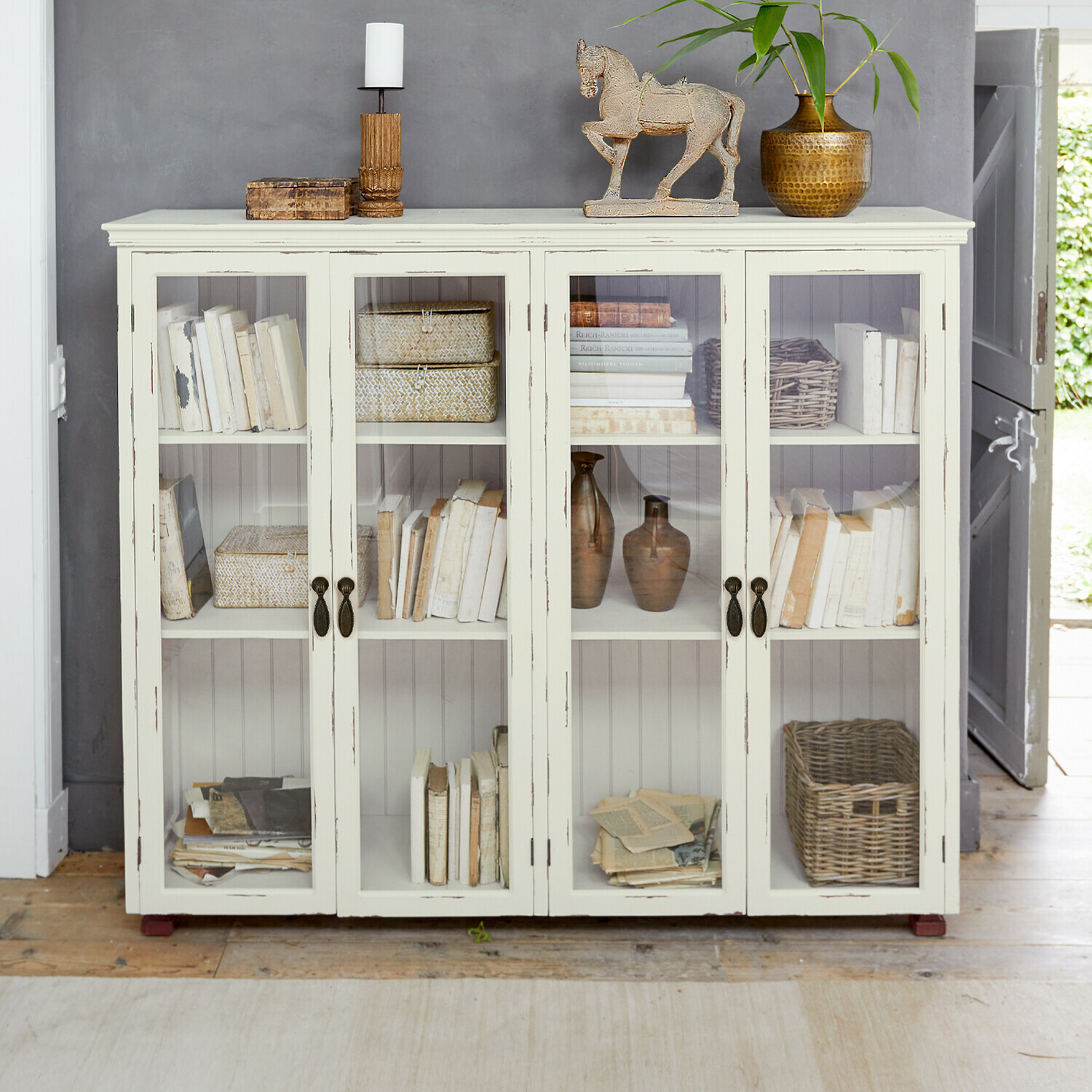Schrank Eastbridge Weiße Holzvitrine mit Glastüren, dekoriert mit Büchern und Vintage-Objekten im Landhausstil