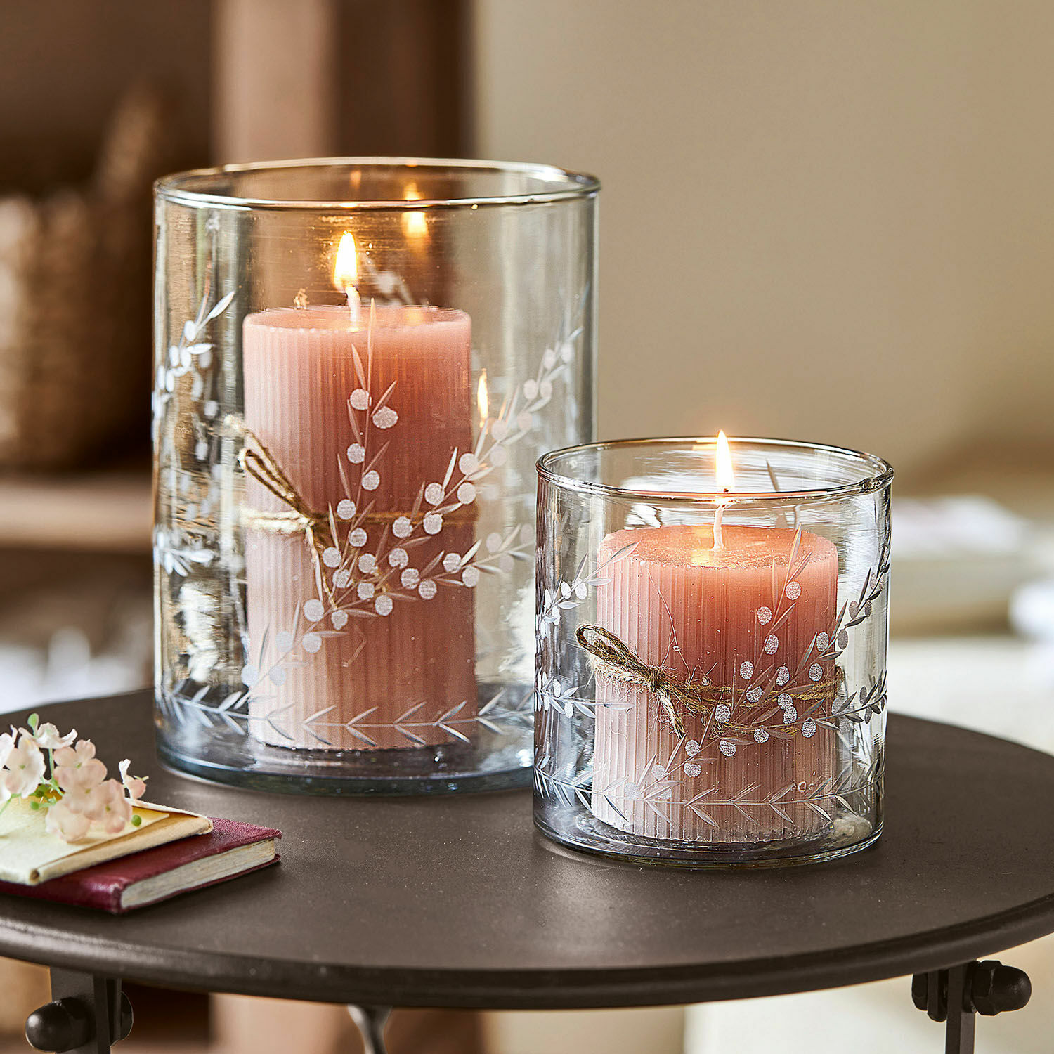 Windlicht 2er Set Temao Zwei rosa Kerzen in transparenten Glaswindlichtern mit weißem Pflanzenmuster auf einem Tisch