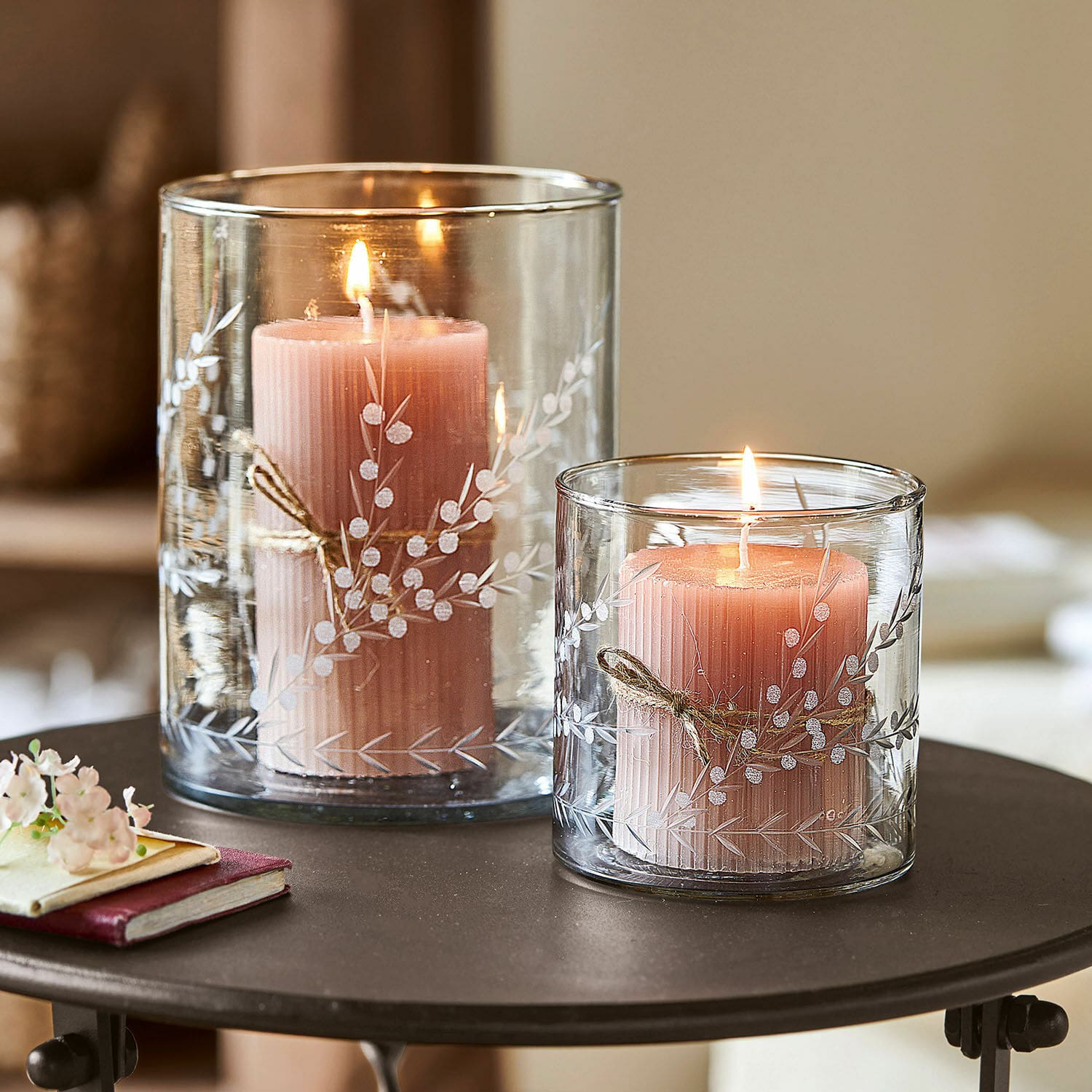 Windlicht 2er Set Temao Zwei rosa Kerzen in transparenten Glaswindlichtern mit weißem Pflanzenmuster auf einem Tisch