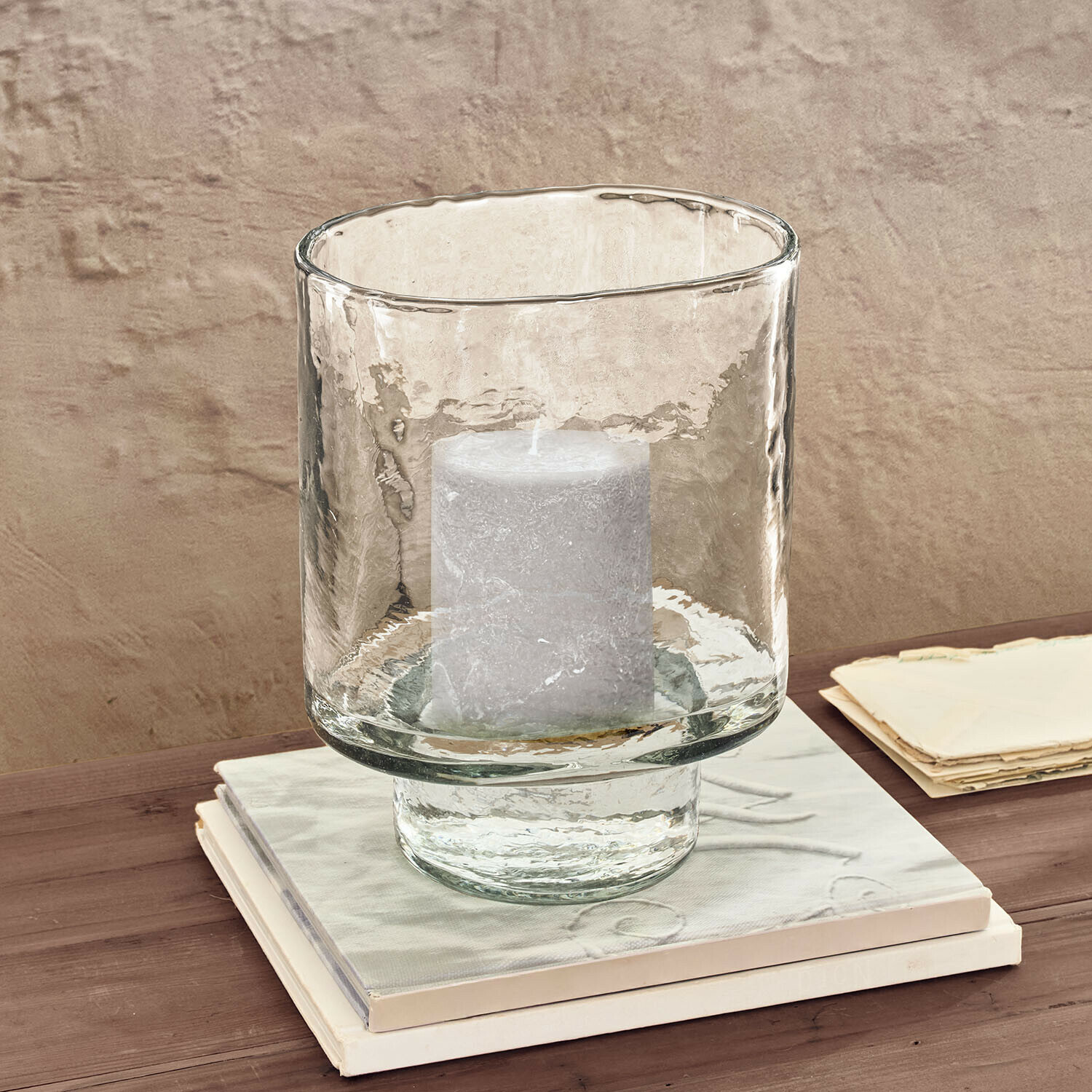 Transparenter Glaswindlicht mit weißer Kerze auf Holztisch neben Büchern