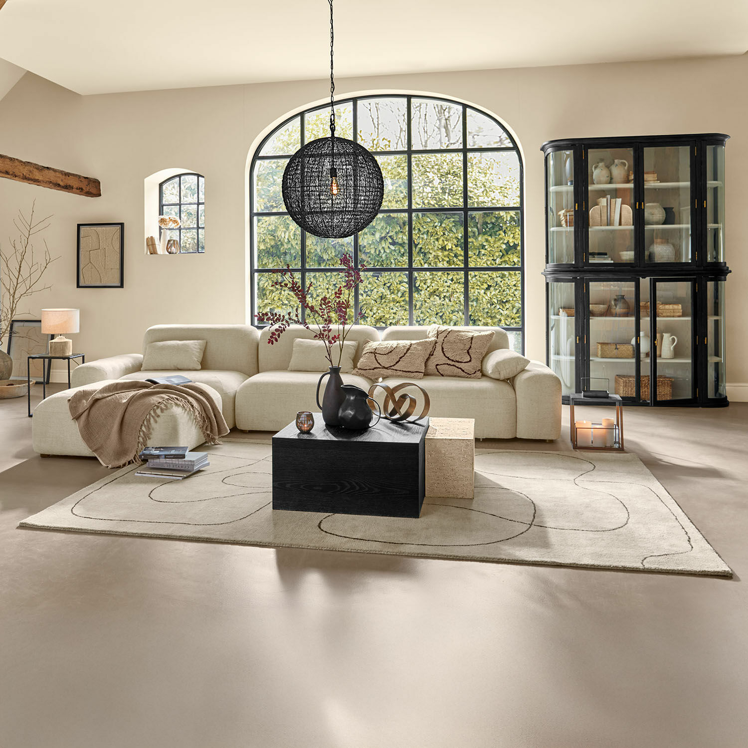 Geräumiges Wohnzimmer mit beigem Stoffsofa, schwarzem Holztisch und großem Fenster mit Blick ins Grüne