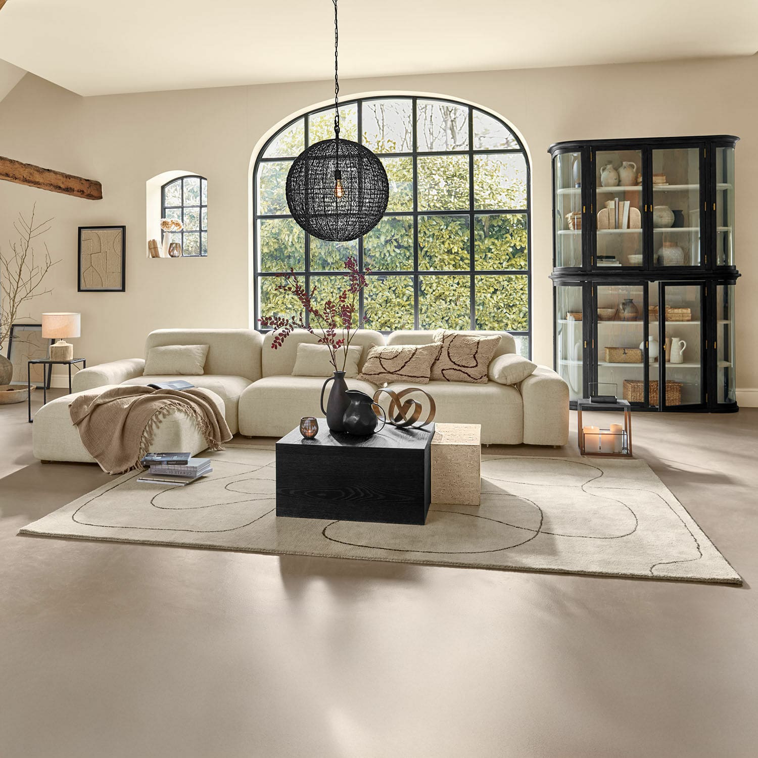 Teppich Lavinois Geräumiges Wohnzimmer mit beigem Stoffsofa, schwarzem Holztisch und großem Fenster mit Blick ins Grüne