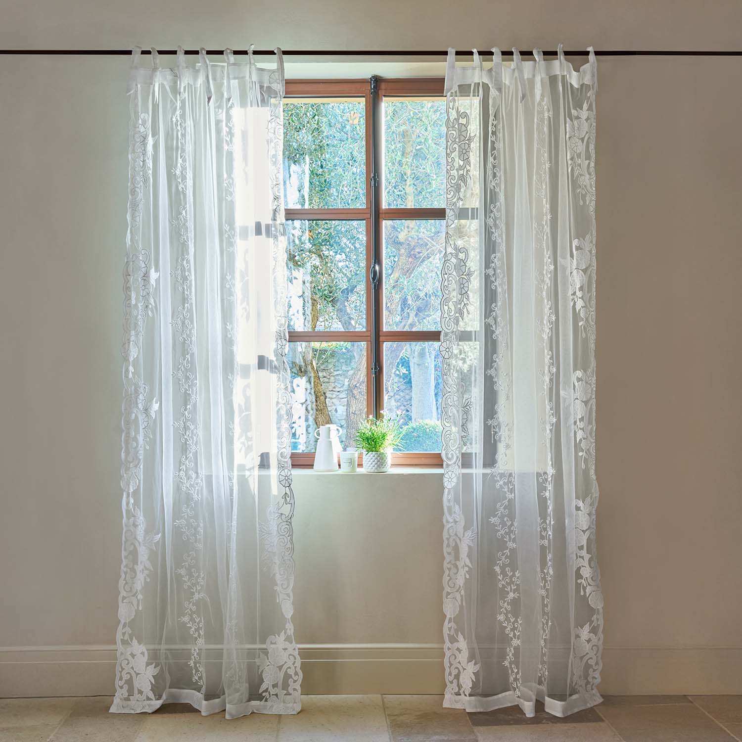 Transparente weiße Gardinen mit besticktem Blumenmuster an einem Holzfenster