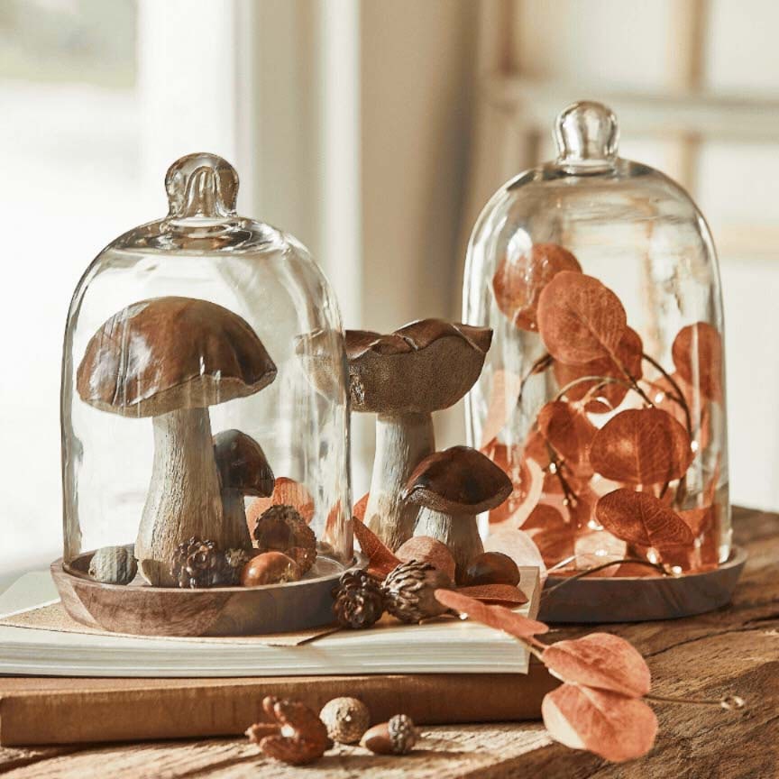 Dekorative Pilze und Blätter unter Glasglocken auf Holzsockel, herbstliche Tischdekoration