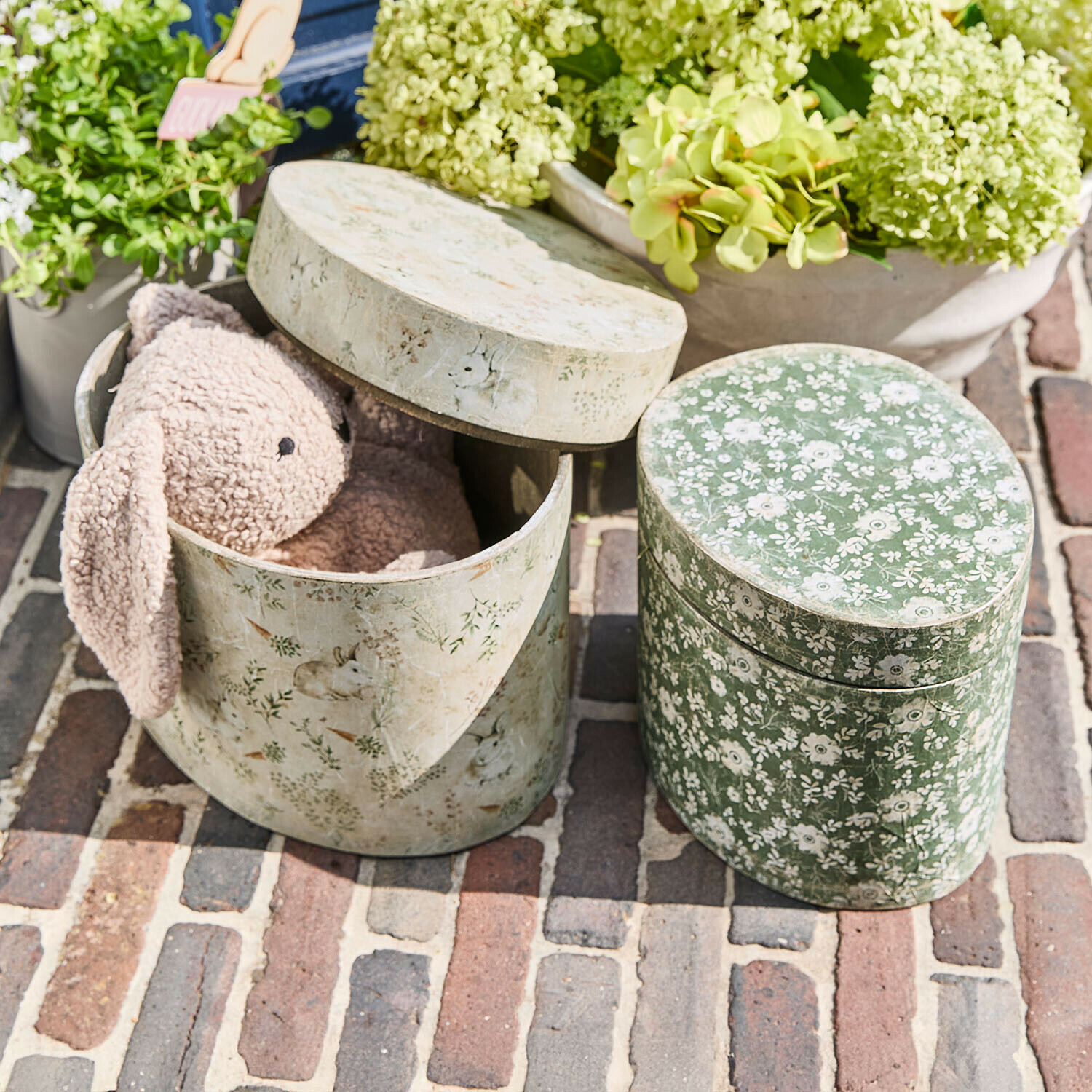 Ovale Dekorationsboxen mit Blumen- und Hasenmotiven, eine mit rosa Plüschhase innen