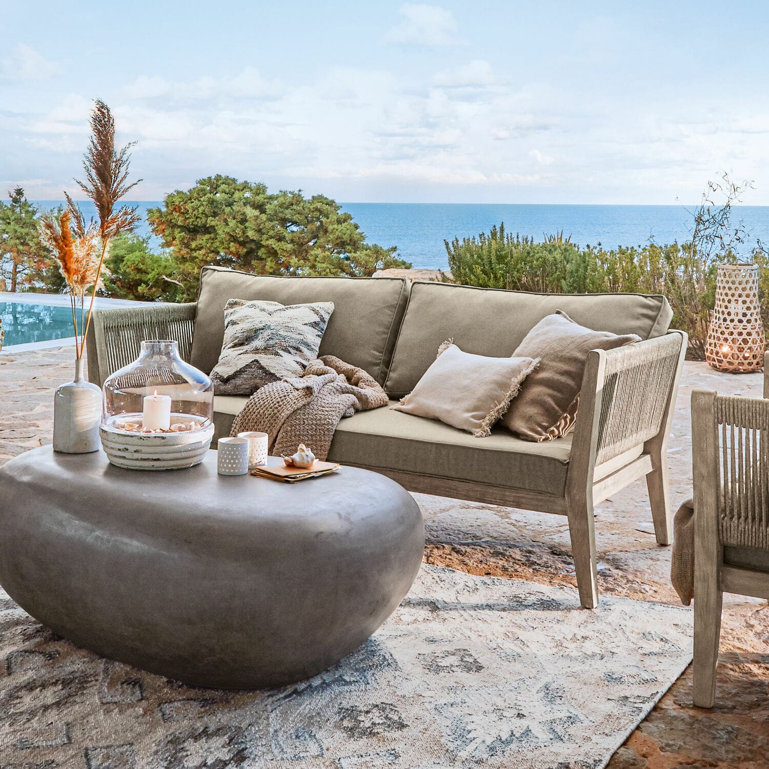Sofa Biarritz Beige Outdoor-Sofa aus Holz und Stoff auf Terrasse mit Meerblick, moderner Steintisch