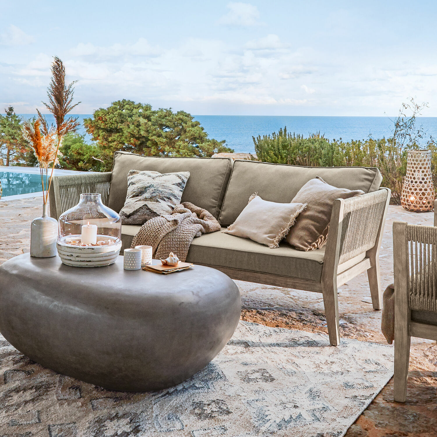 Sofa Biarritz Beige Outdoor-Sofa aus Holz und Stoff auf Terrasse mit Meerblick, moderner Steintisch