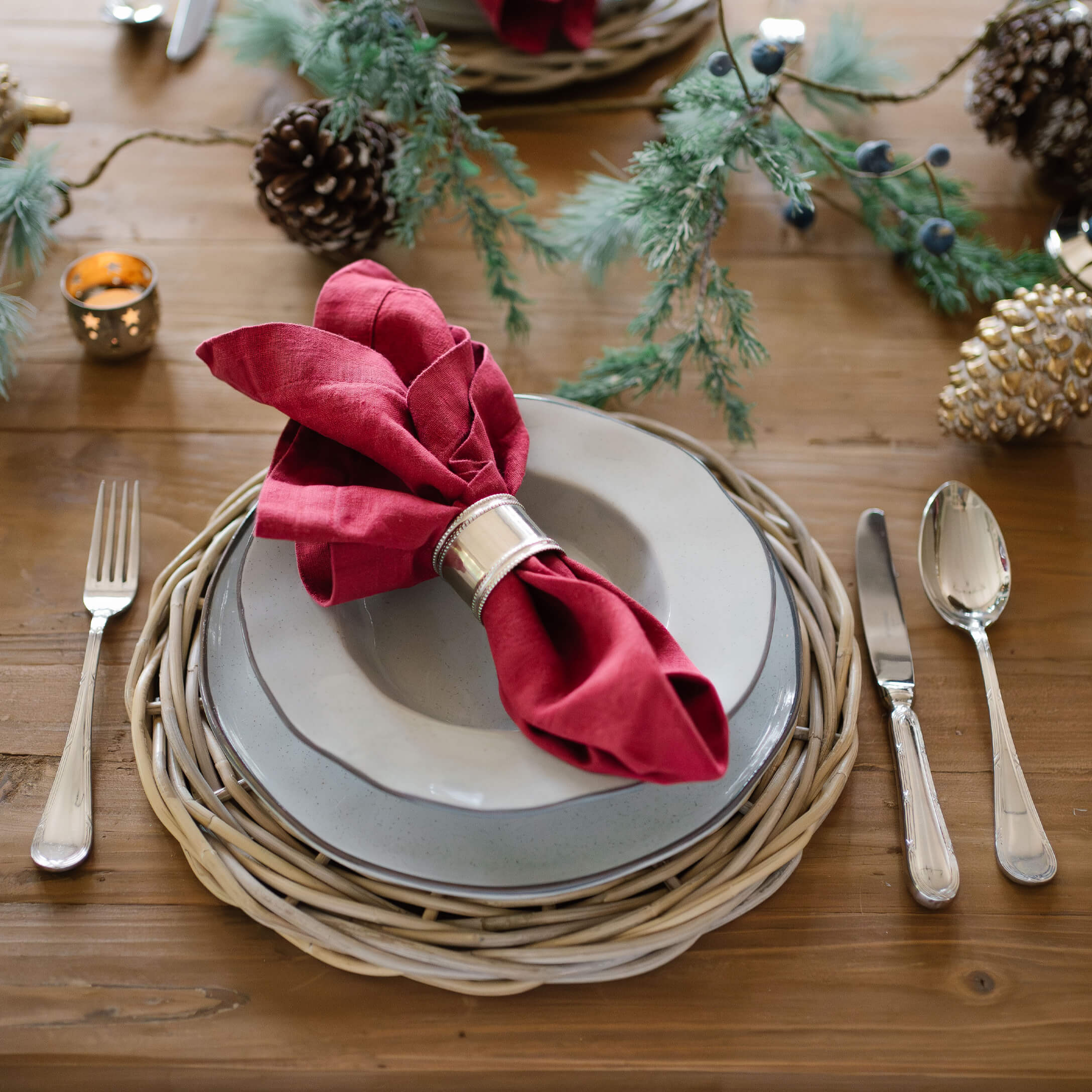 Elegantes Tischgedeck mit grauen Tellern, rotem Leinenserviettenring und natürlichem Weidenuntersetzer