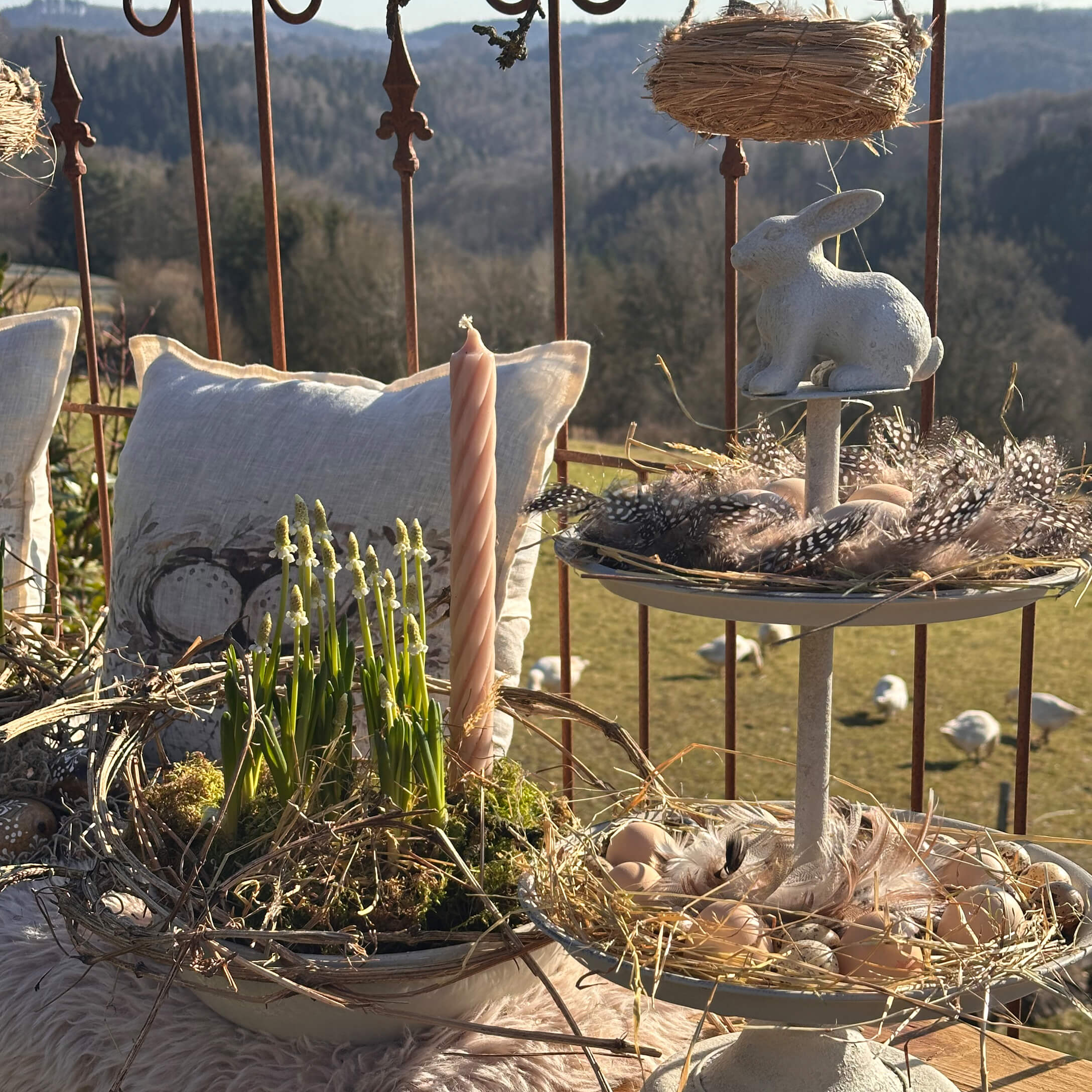 Natürliche Osterdekoration mit weißem Hasen, Federn und Kerze auf rustikalem Hintergrund mit Kissen
