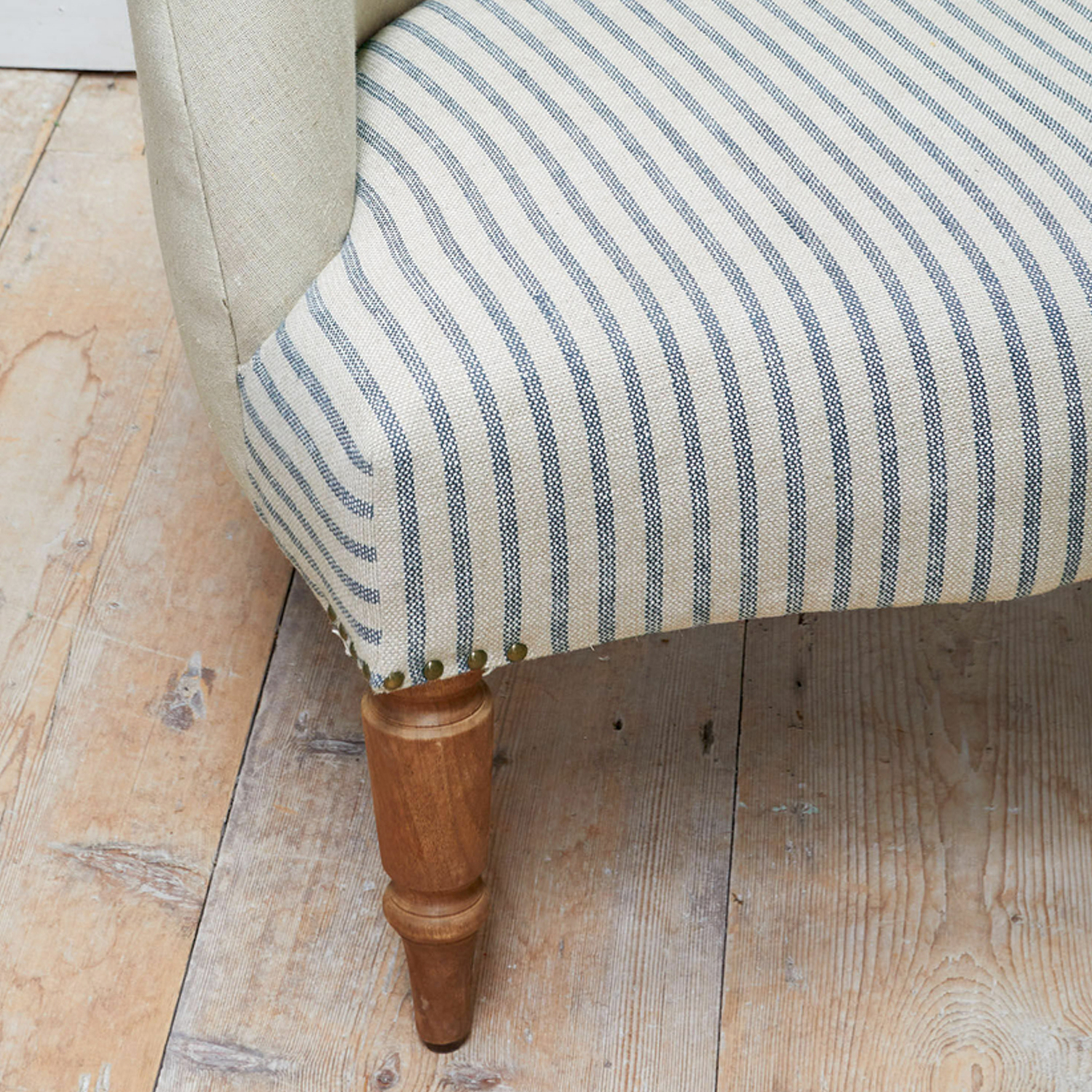 Holzbein eines Möbelstücks mit beige-blau gestreiftem Stoffbezug auf Holzboden