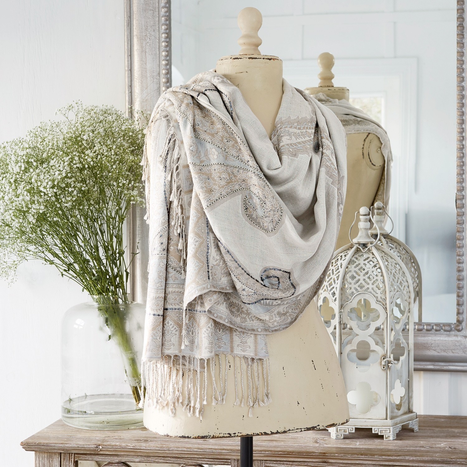 Schal Moyra Beiger Schal mit Paisley-Muster und Fransen auf Schneiderpuppe, Dekoration mit Laterne und Blumen
