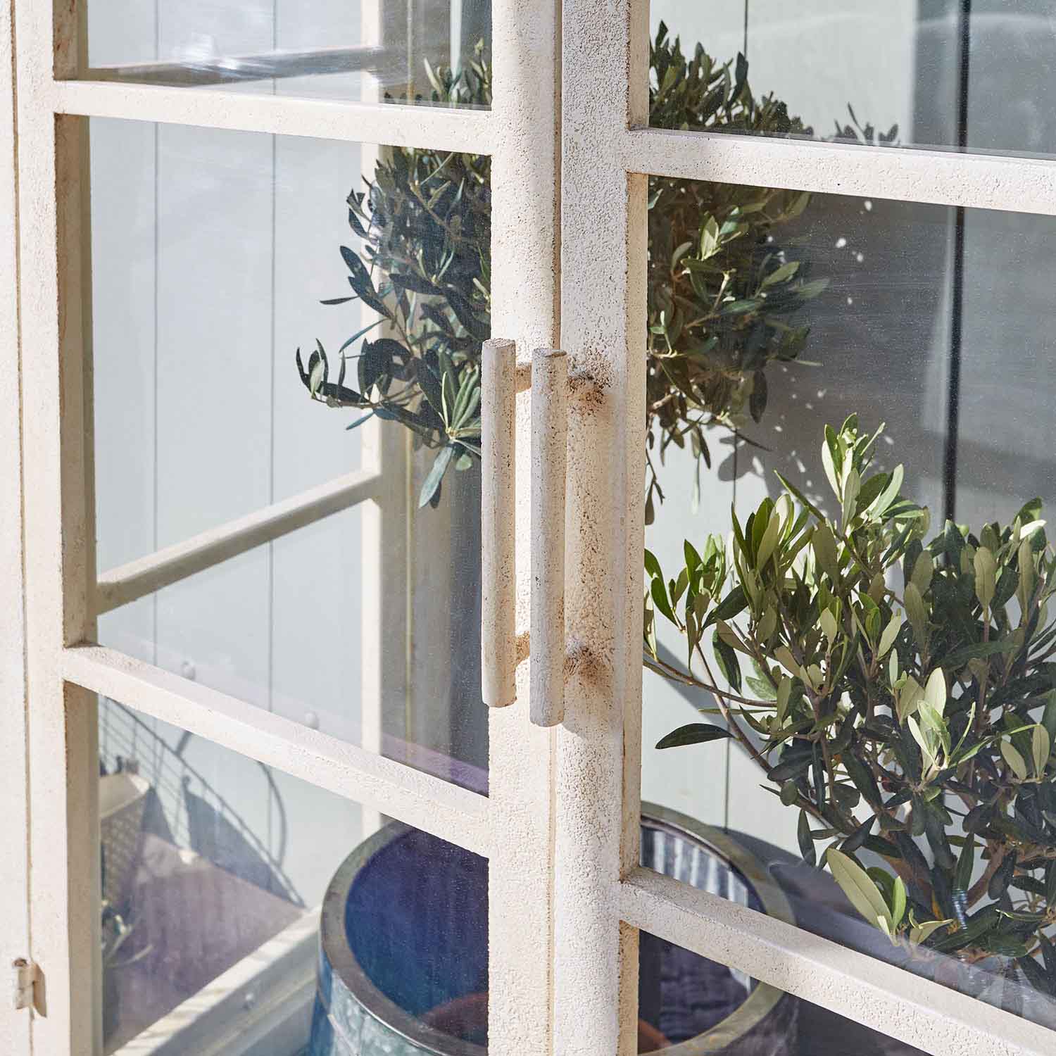 Weiße Metalltür mit Griffen und grünen Pflanzen im Hintergrund, Gartendekoration