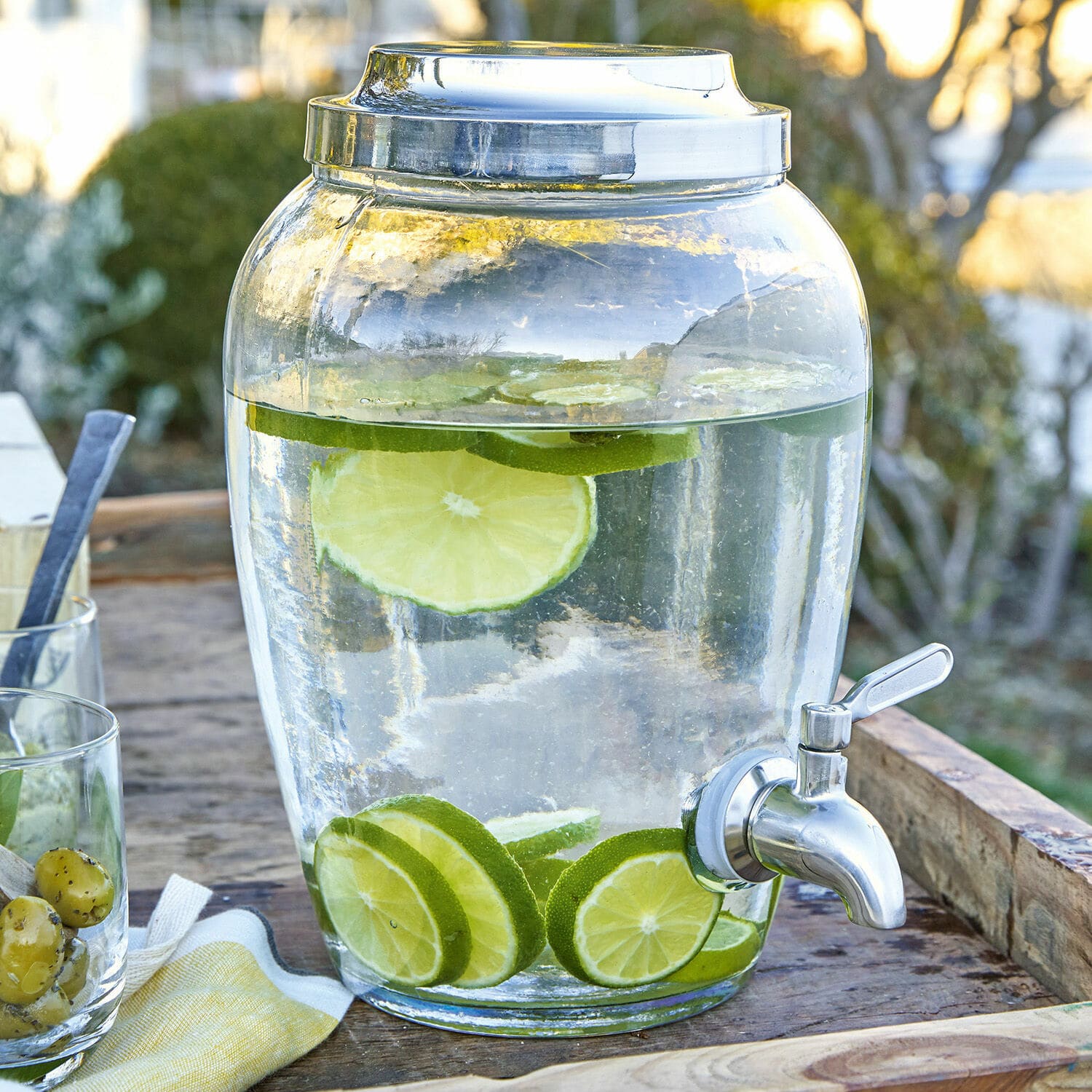 Glasgetränkespender mit Zapfhahn, Wasser mit Limettenscheiben auf rustikalem Holztisch