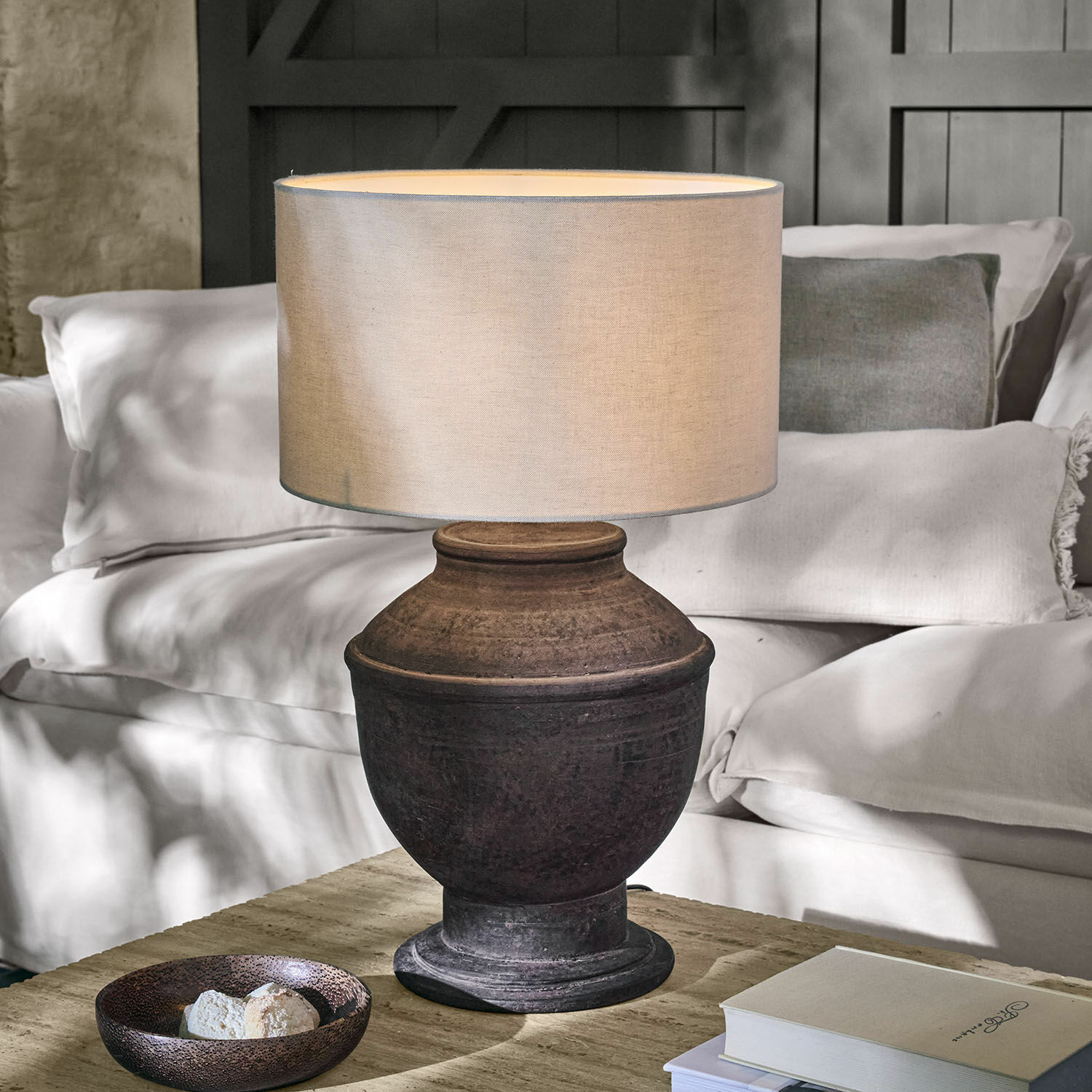 Tischlampe aus dunkler Keramik mit beigem Lampenschirm auf Holztisch im Wohnzimmer