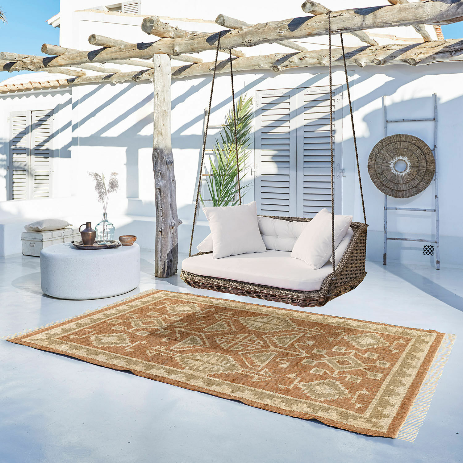 Teppich Serenath Braun-beigefarbener Teppich mit geometrischem Muster auf hellem Balkon mit Rattanschaukel und Kissen