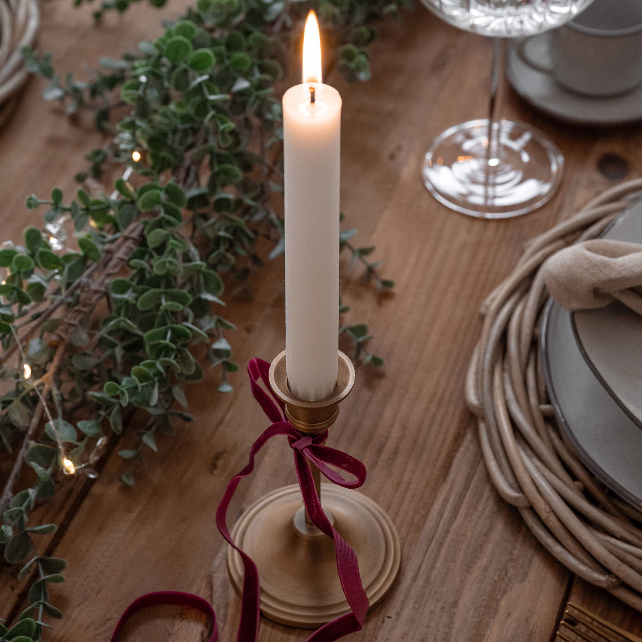Goldener Kerzenhalter mit weißer Kerze und rotem Samtband auf Holztisch mit Weihnachtsdeko