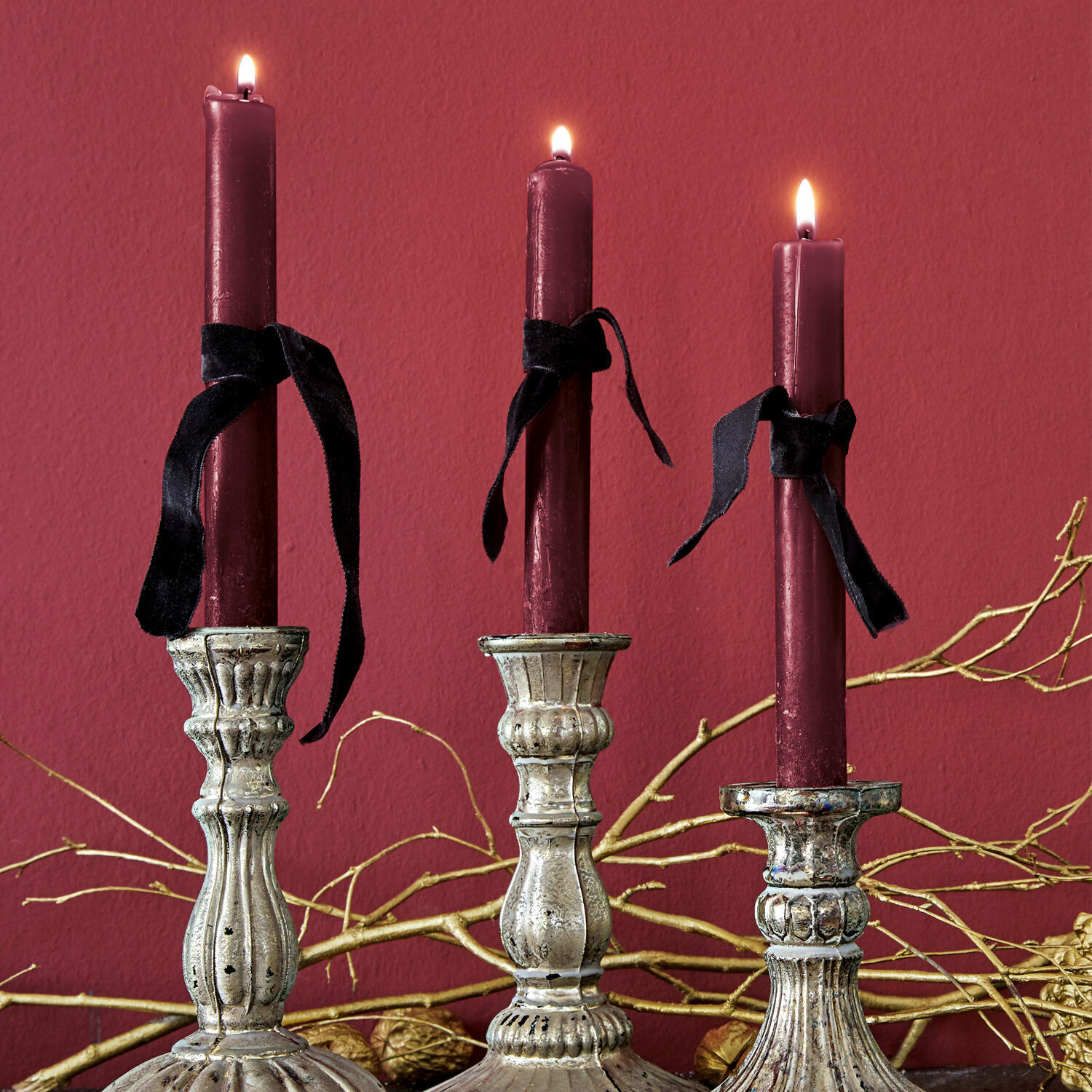 Kerze 12er Set Bauceau Drei silberne Metallkerzenhalter mit bordeauxfarbenen Kerzen und schwarzen Bändern vor rotem Hintergrund