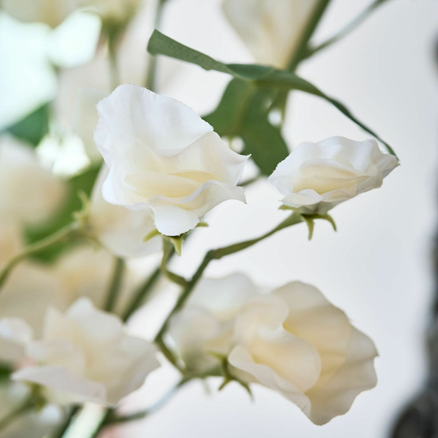 Zarte weiße Stoffblumen mit grünen Stielen als dekorative Innenraumgestaltung