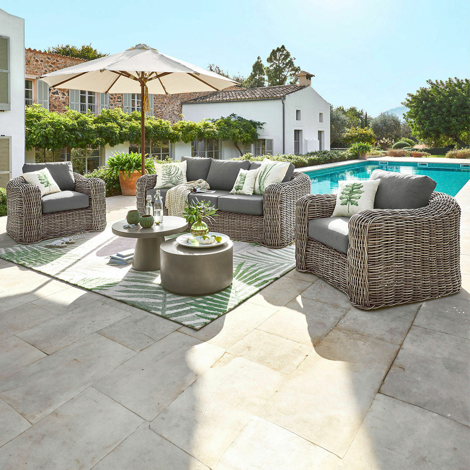 Sitzgruppe Upminster Gartenmöbel-Set aus grauem Technorattan mit Kissen und Sonnenschirm neben dem Pool