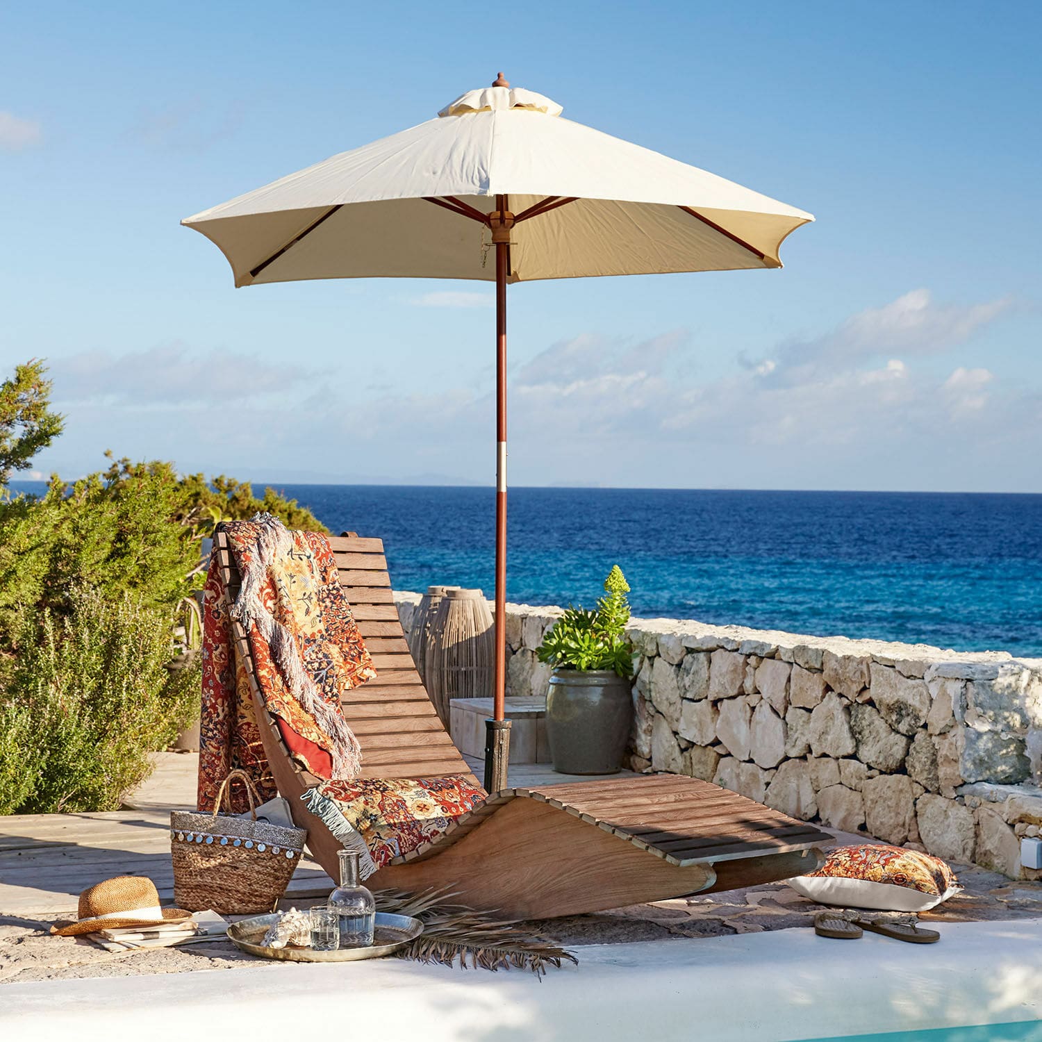 Lounger Wenham Holzliege mit cremefarbenem Sonnenschirm und buntem Plaid am Pool mit Meerblick
