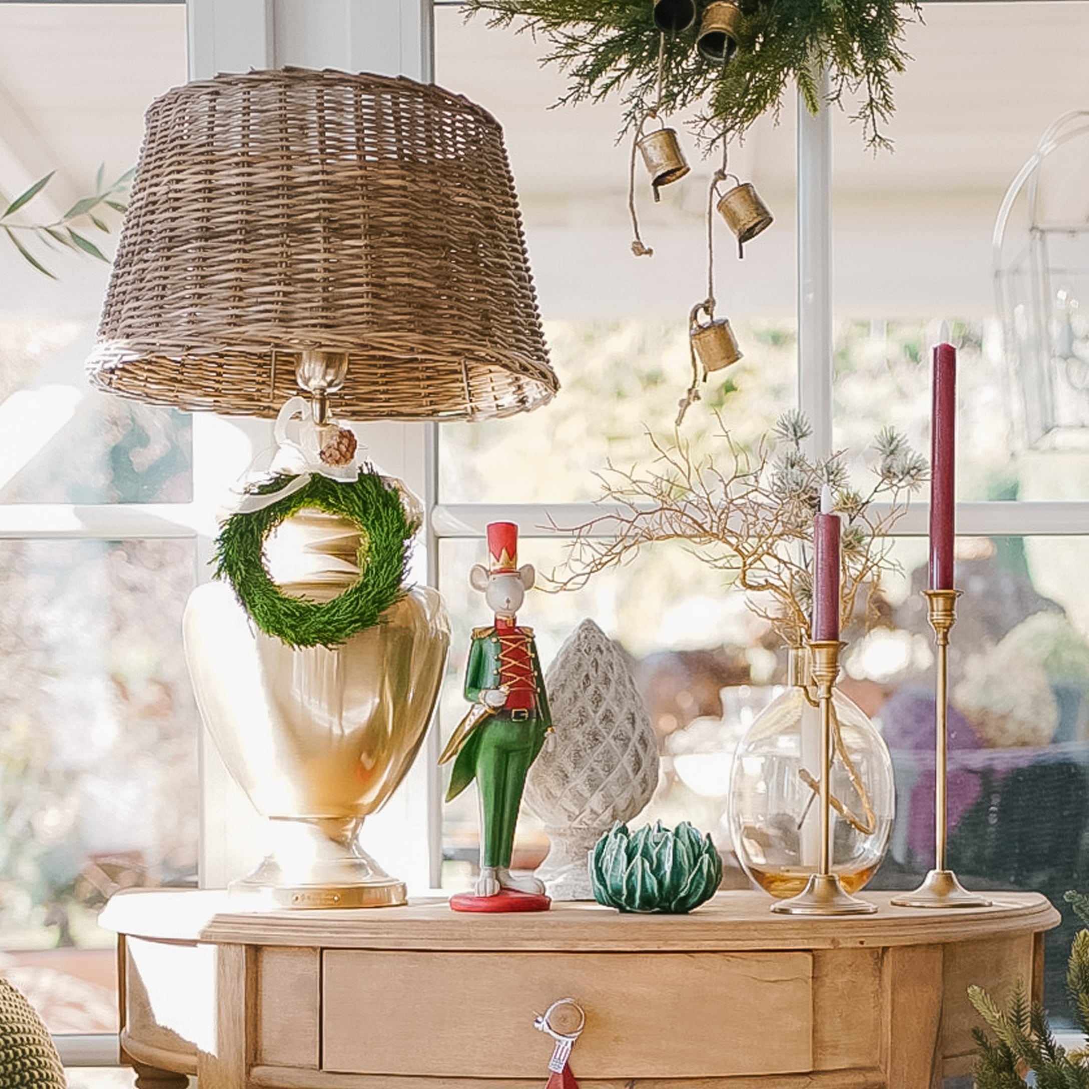 Dekorative Lampe mit Korbgeflecht-Schirm und Weihnachtsdeko auf hellem Holztisch im sonnigen Raum