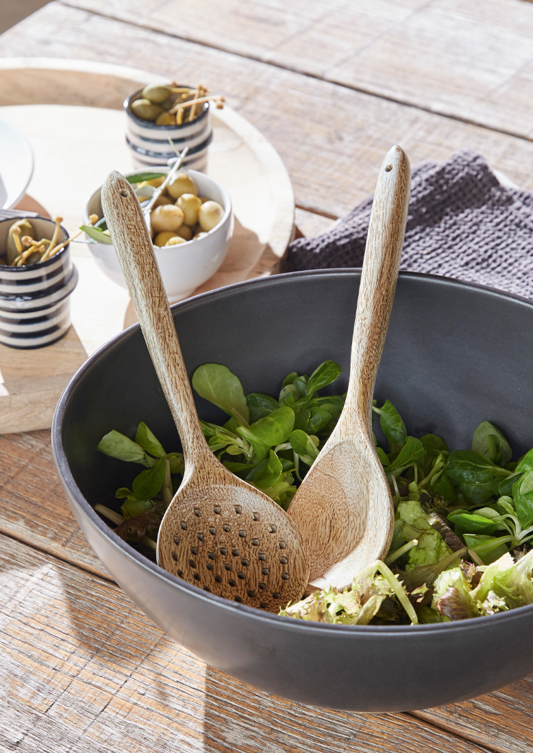 Schwarze Salatschüssel mit Holzlöffeln und frischem grünem Salat auf Holztisch