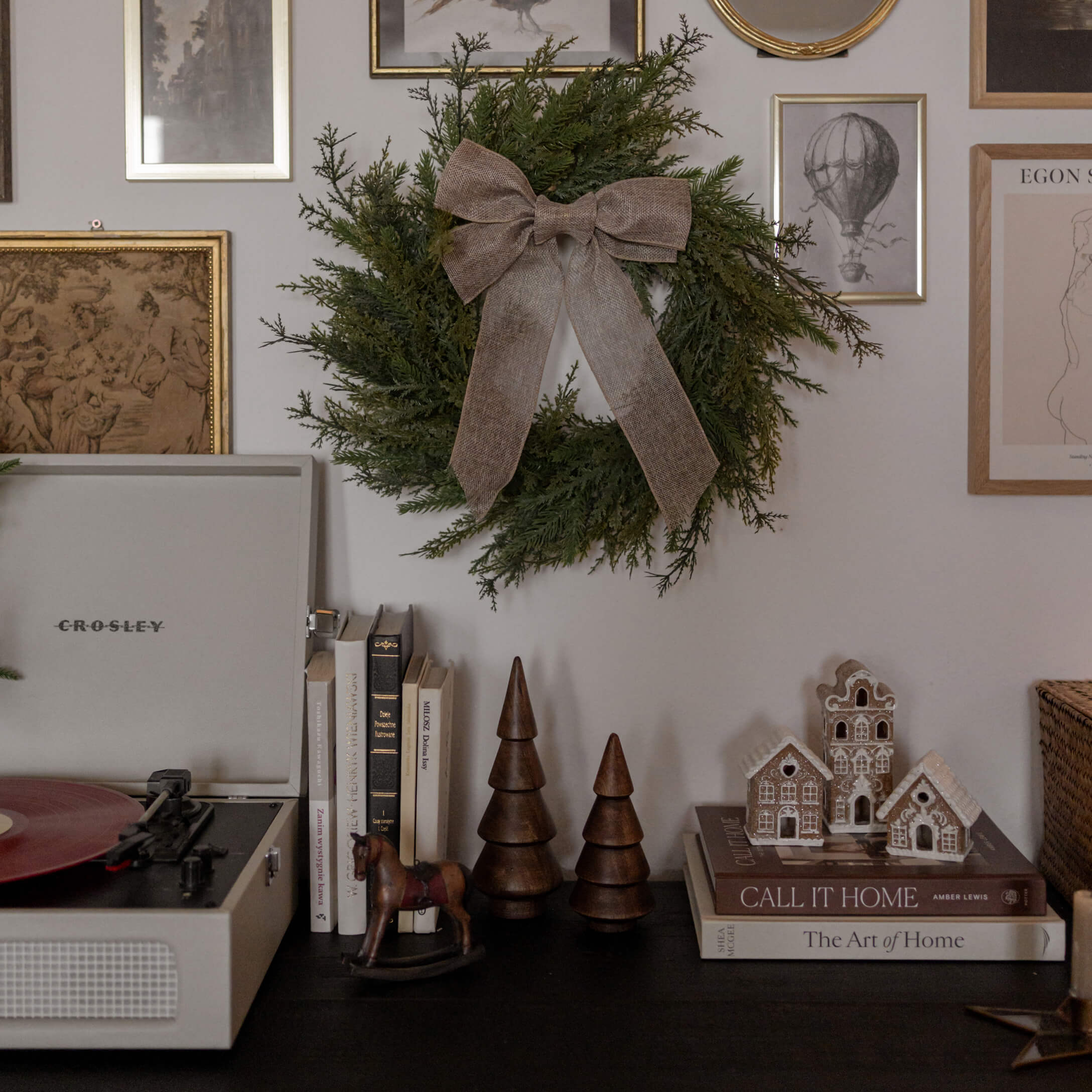 Grüner Dekokranz mit brauner Schleife an Wand über schwarzer Ablage mit Büchern und Holzfiguren