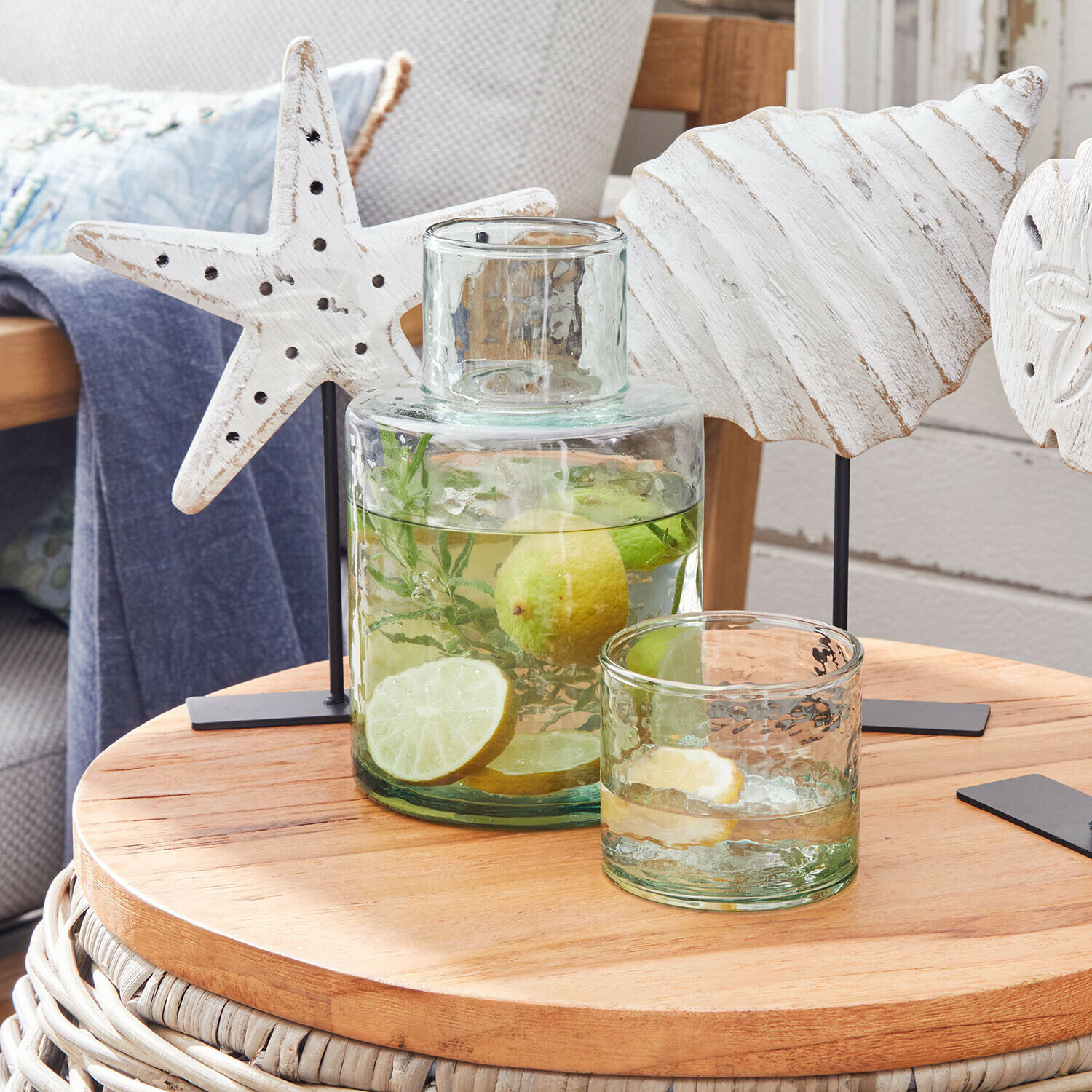 Glaskaraffe und Glas mit Wasser, Limette und Zitrone auf Holztisch mit maritimen Dekorationen