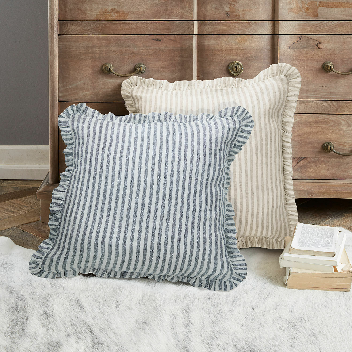 Kissenhülle 2er Set Brenda Zwei dekorative Kissen mit Streifen und Rüschen in Beige und Blau auf Teppich vor Holzkommode