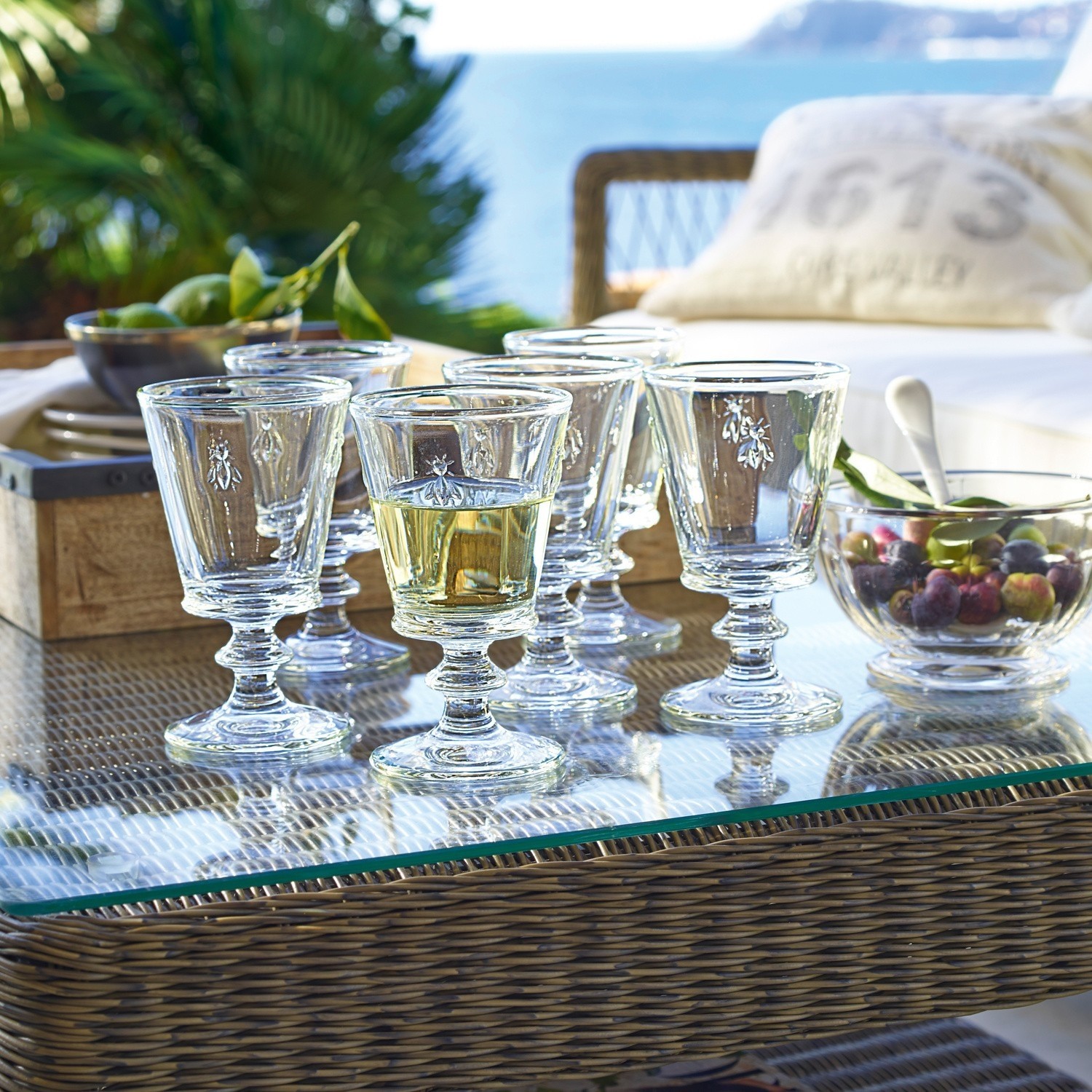 Sechsteiliges Set Gläser aus Glas mit Insektenmotiv auf Glastisch auf Terrasse mit Meerblick