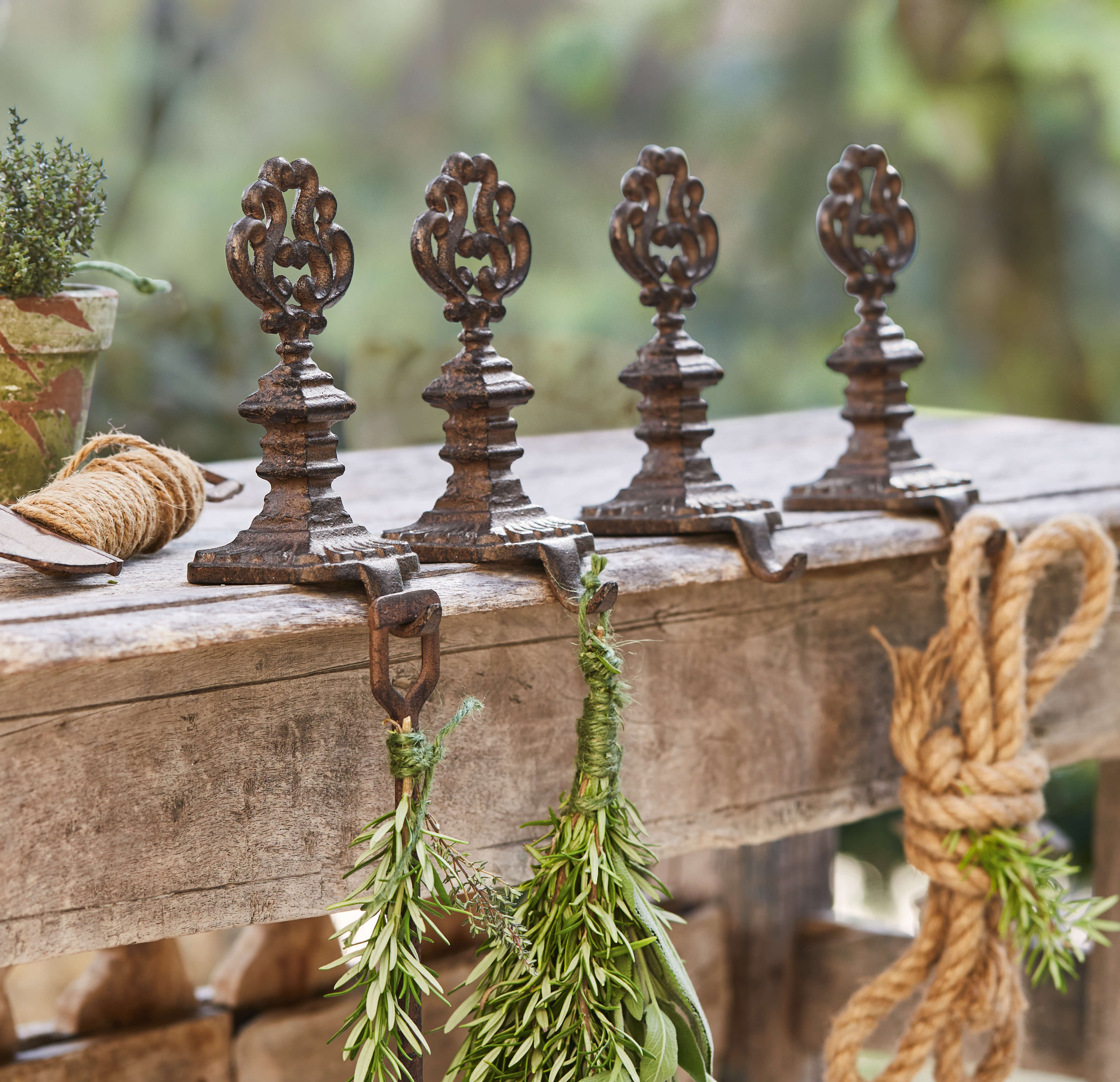 Vier dekorative Vintage-Gusseisenhaken auf Holztisch mit frischen grünen Kräutern
