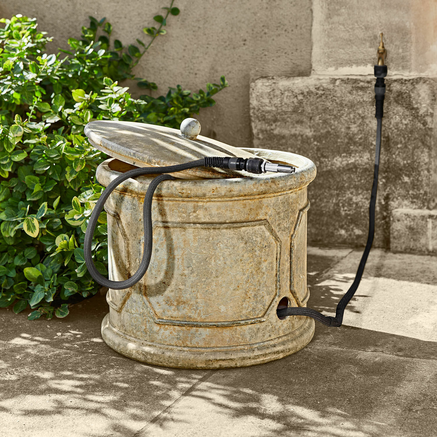 Gartenschlauchtopf Filervo Runder Gartenbehälter aus beigem Stein mit schwarzem Gartenschlauch zum Bewässern