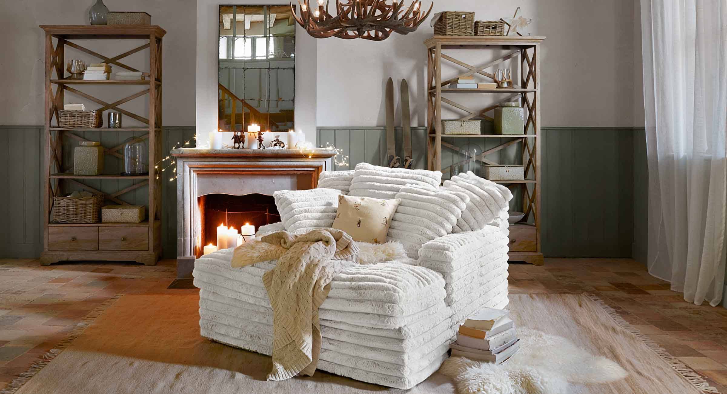 Gemütlicher weißer Sessel aus weichem Material im Chalet-Stil mit Kamin und Holzregalen im Wohnzimmer