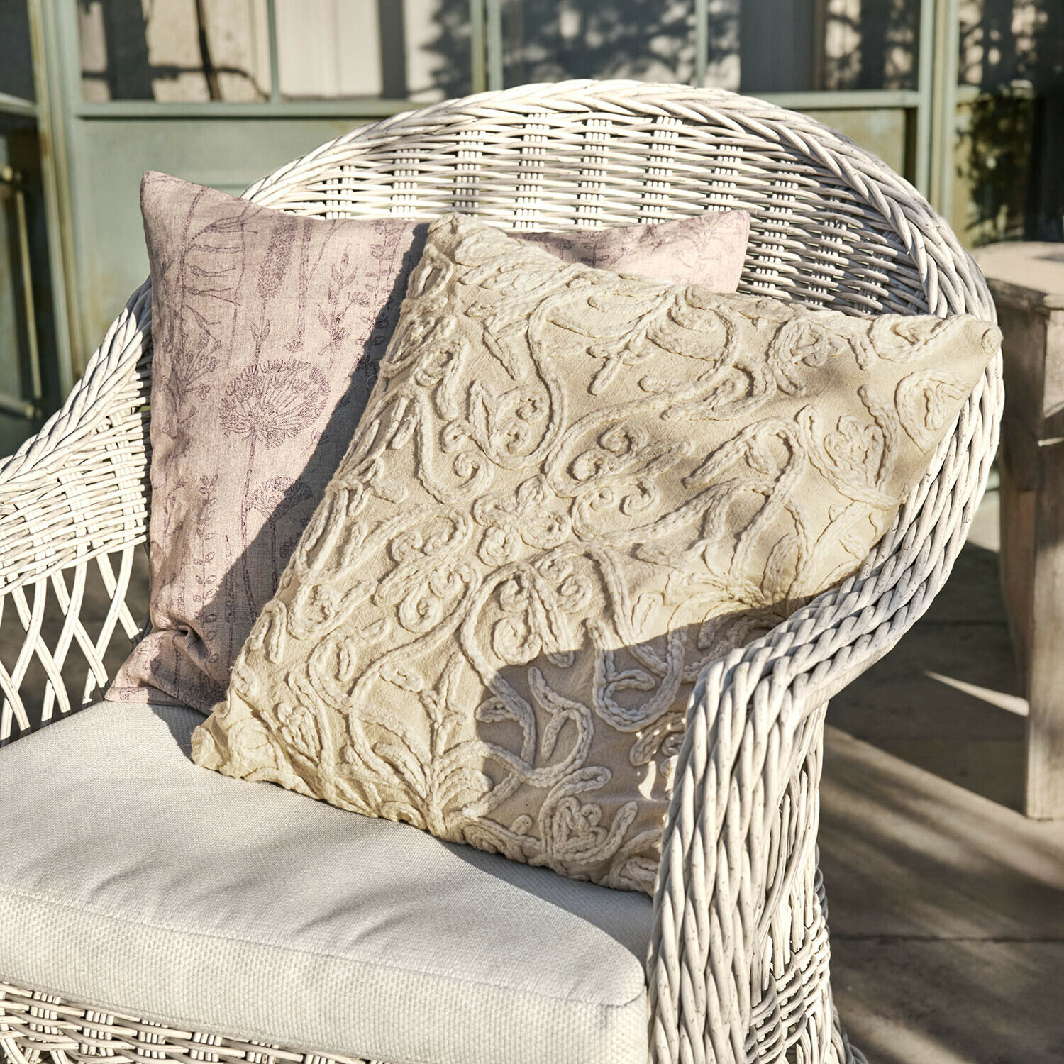 Zwei dekorative Kissen in Beige und Rosa auf einem weißen Korbsessel auf der Terrasse