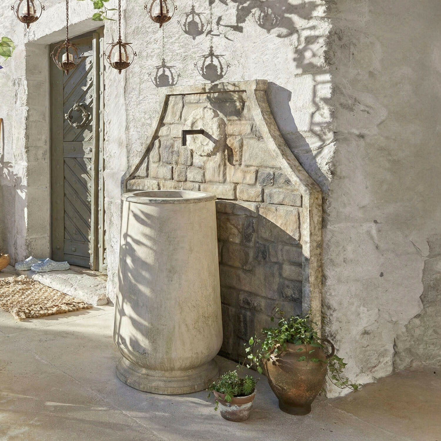 Dekorativer beiger Steingartenbrunnen mit rustikalem Wasserhahn und Pflanzgefäßen daneben